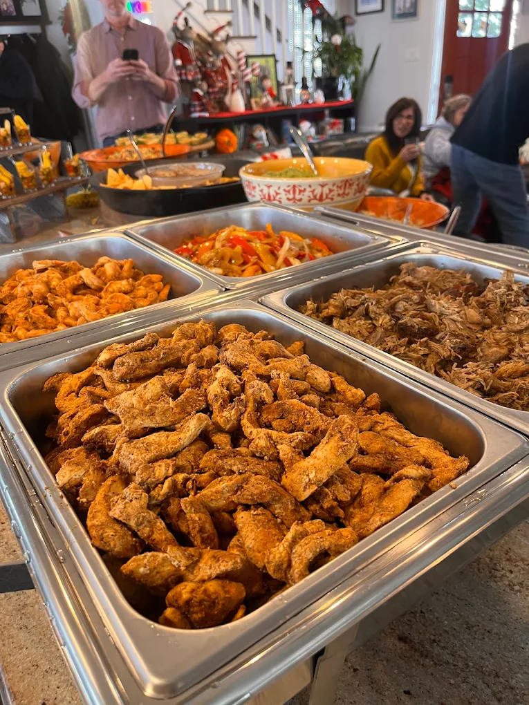 Buffet table with trays of fried chicken, beef, and vegetables, in a busy indoor setting with people in the background.