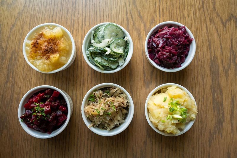 Six small bowls of different colored food on a wooden surface, arranged in two rows of three.