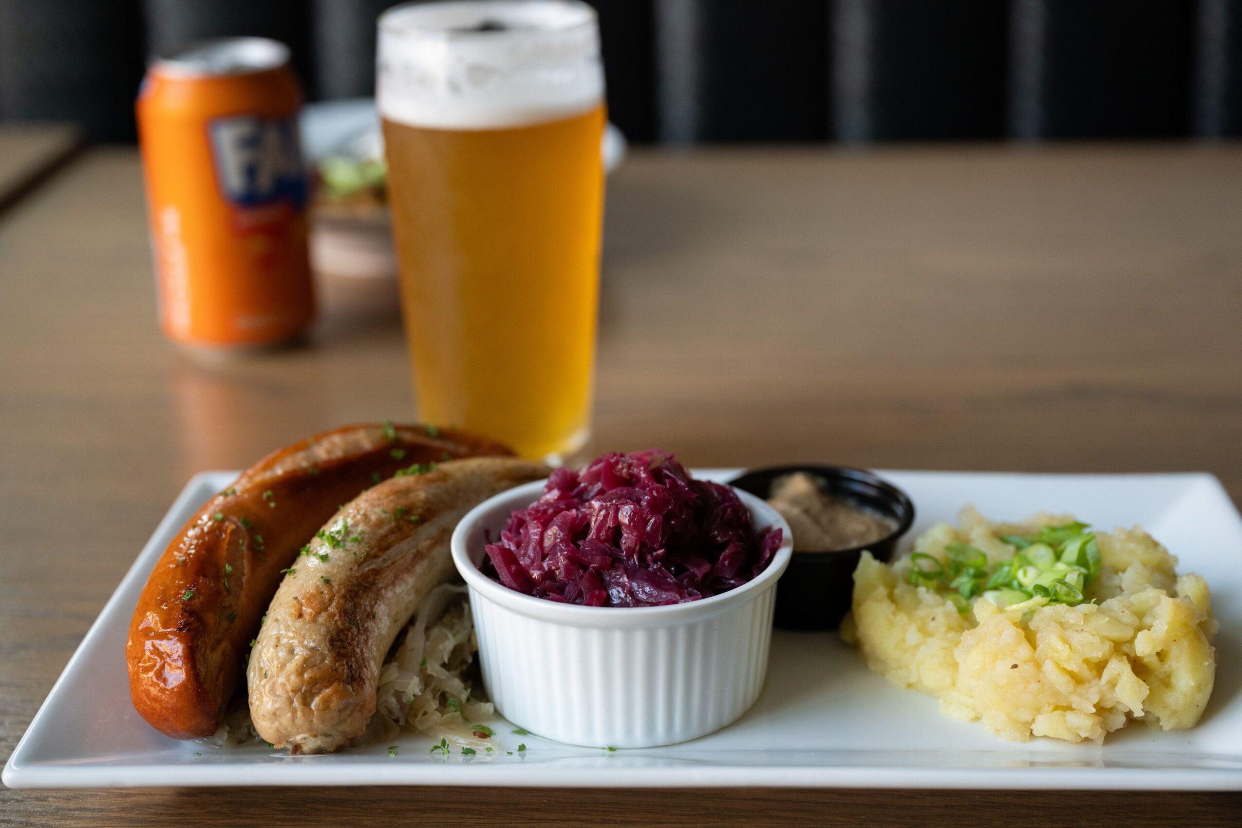 Plate with sausage, mashed potatoes, and beet salad, with a glass of beer and a can in the background.
