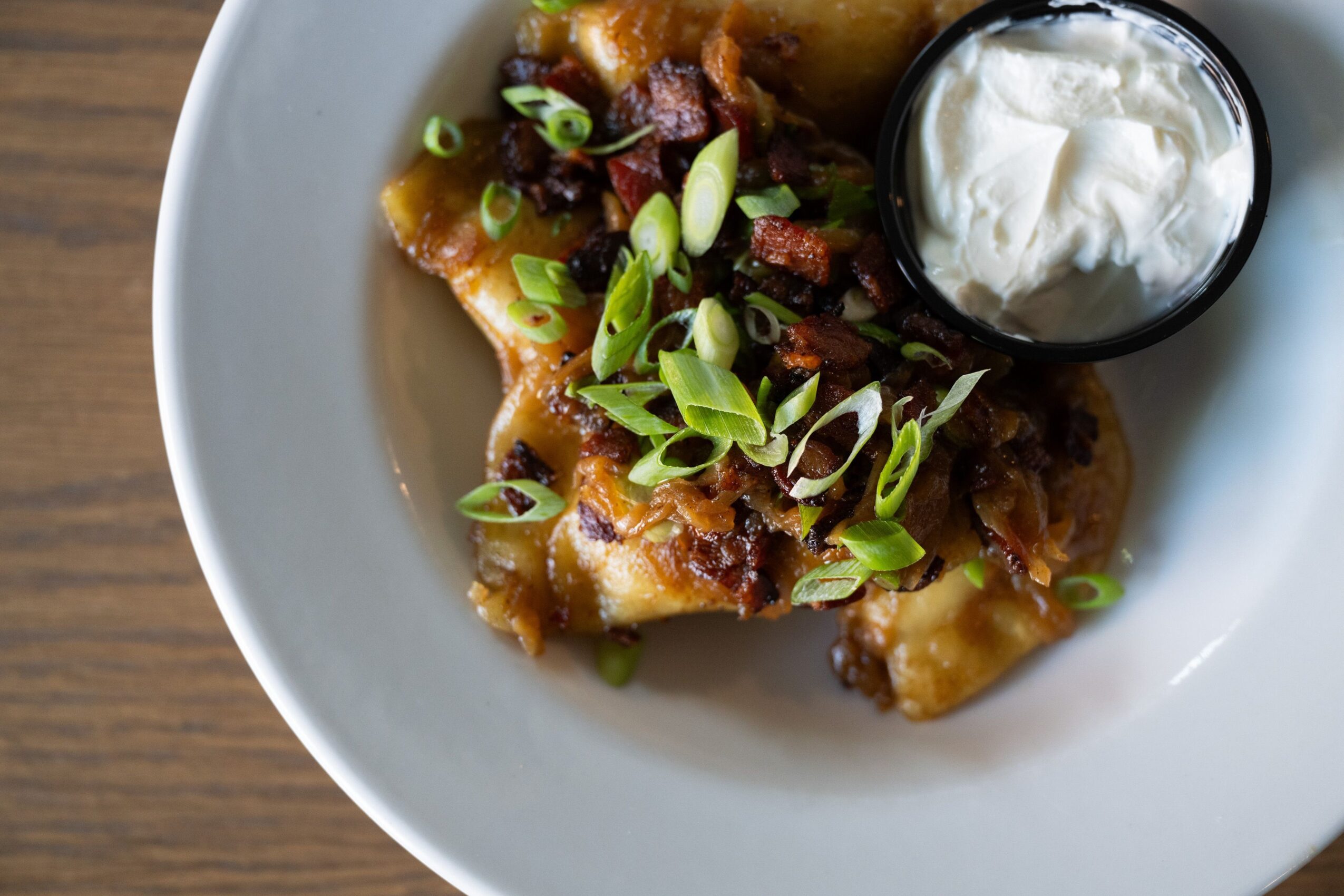 Plate with food, topped with chopped green onions and a side of sour cream, on a wooden surface.