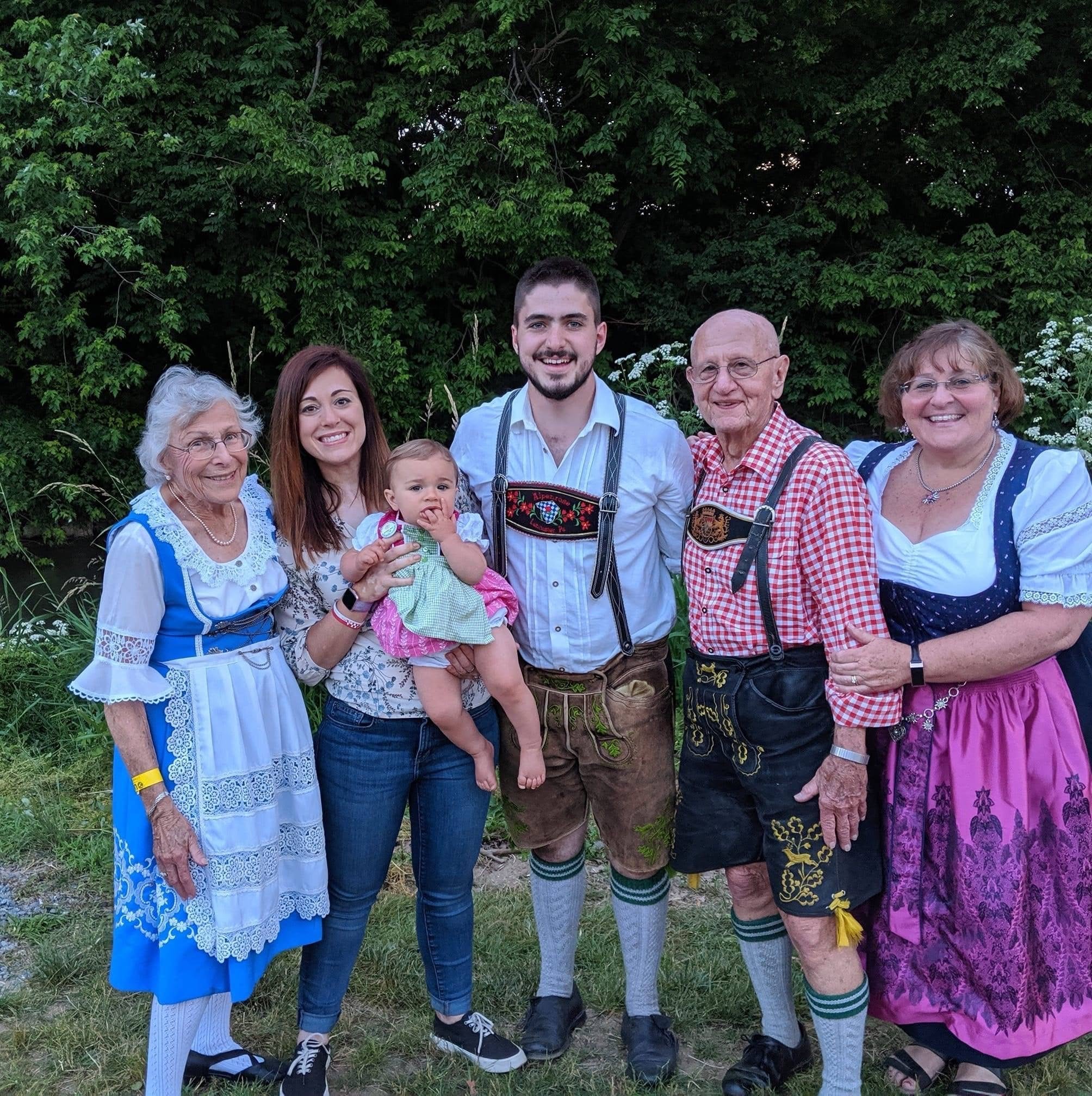Group of six people, including children, standing outdoors with trees in background, smiling for the photo.
