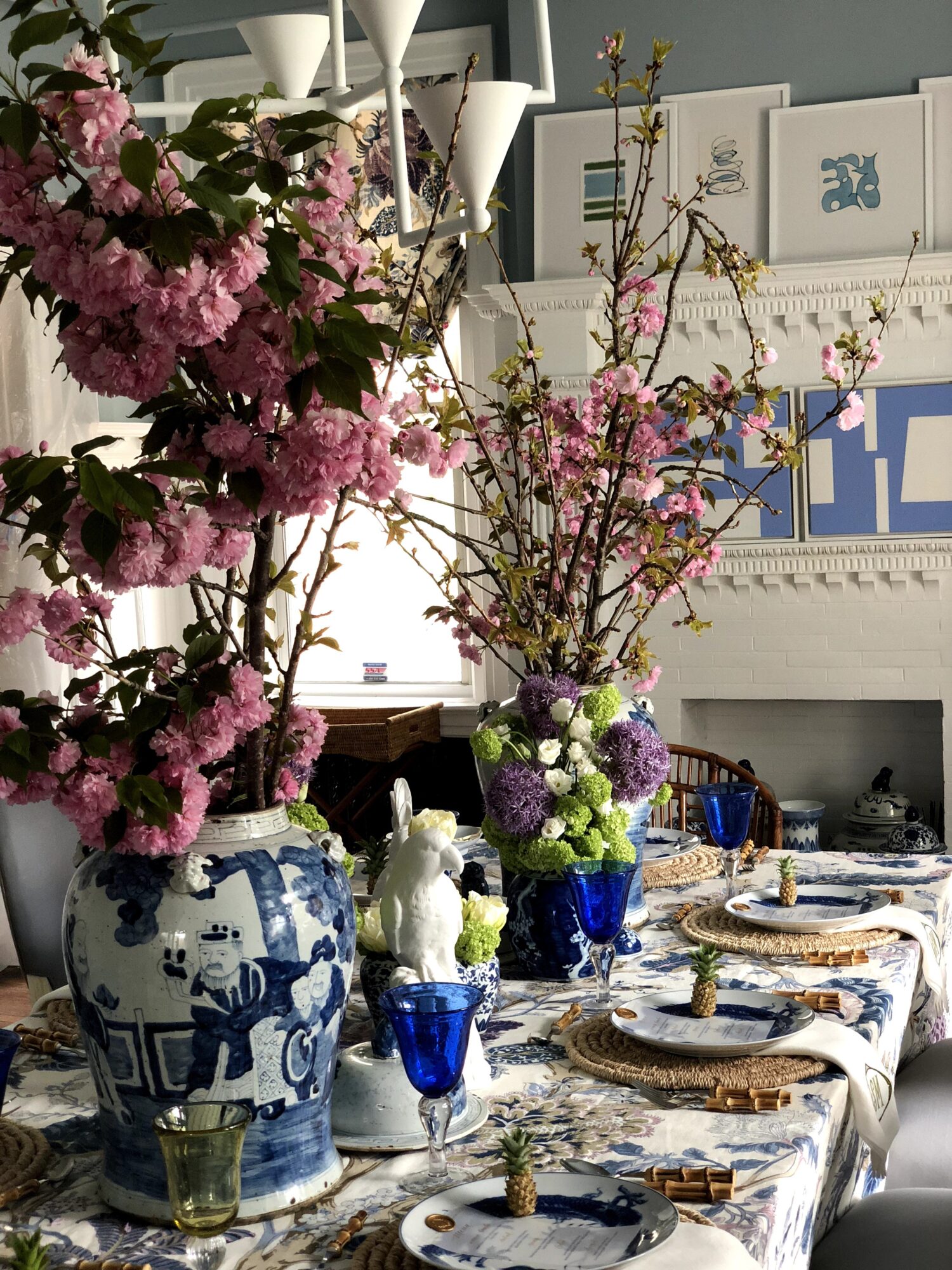 Dining table with floral arrangements in vases, set with plates, glasses, and cutlery, in a decorated room.