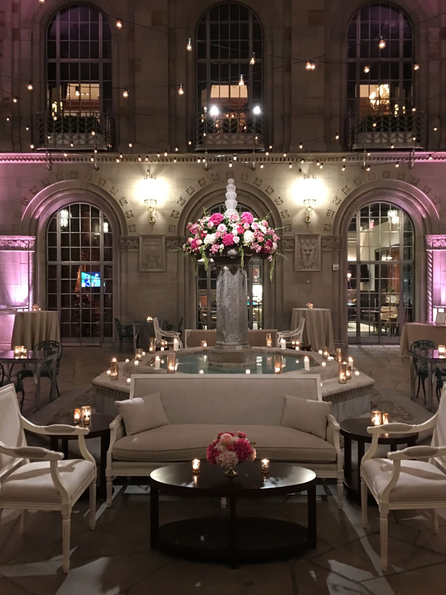 Elegant dining room with a long table, floral centerpiece, candles, and large windows with draped curtains, illuminated by chandeliers.