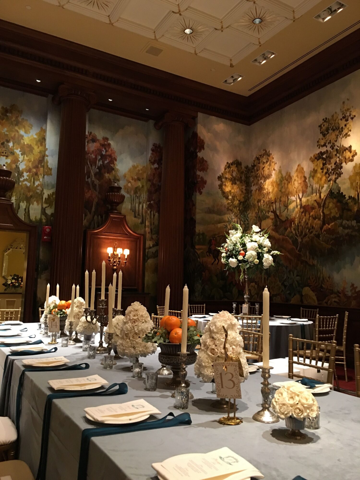 Elegant table setting with floral centerpiece, candles, and decorative items in a decorated room with a mural of trees.