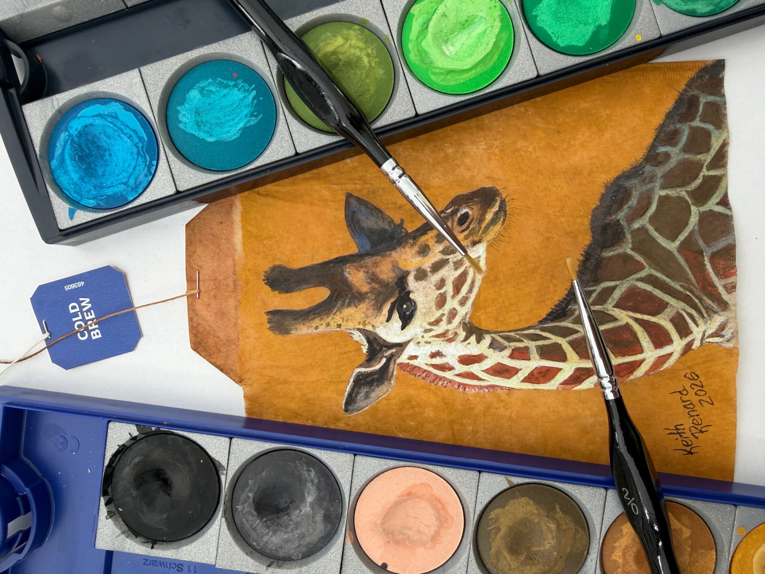 Paintbrushes and watercolor paints on paper with a giraffe illustration, including a giraffe's head and neck, on an orange background.
