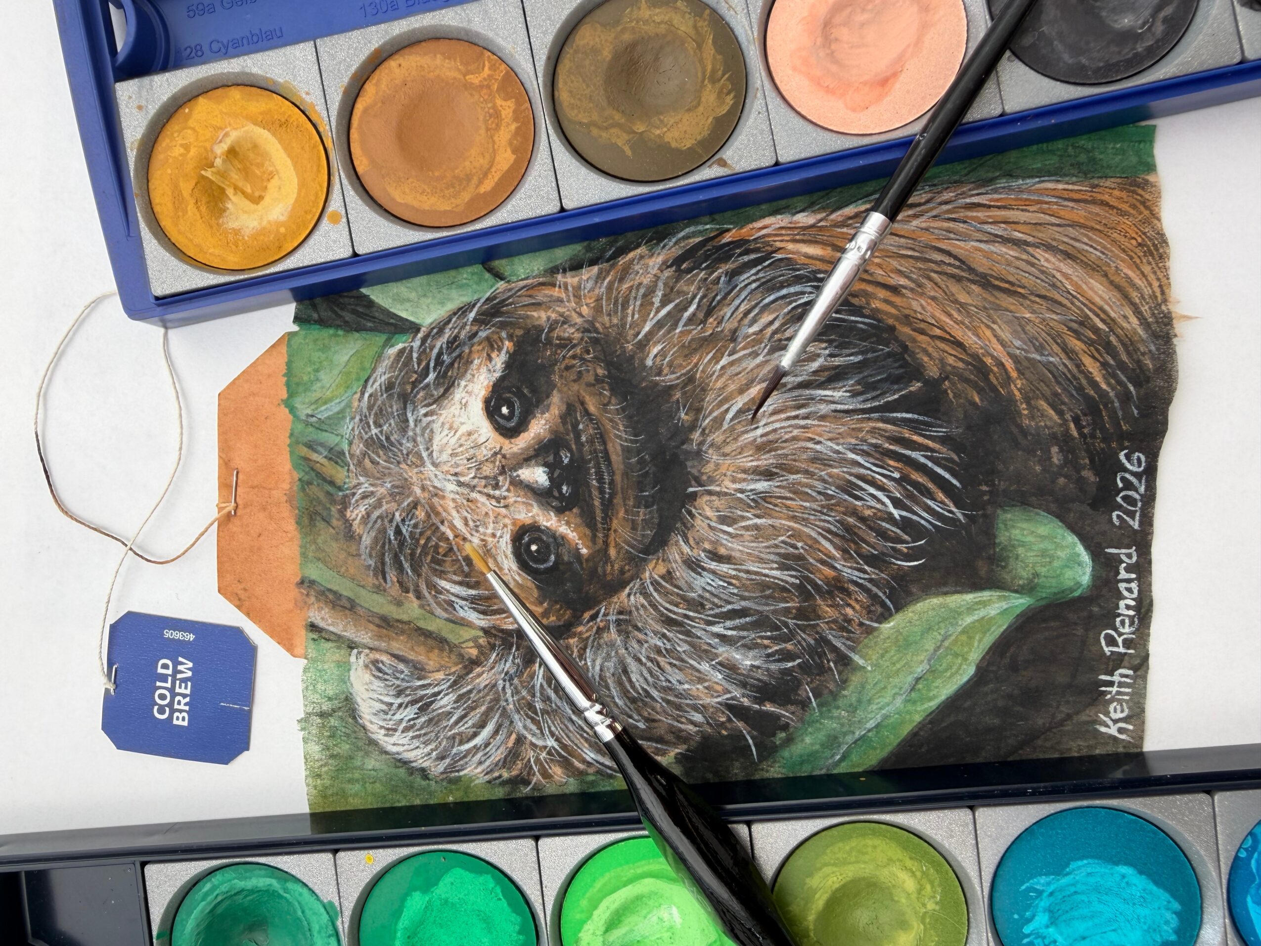 A realistic watercolor painting of a guinea pig with brown, black, and white fur, lying on green leaves, with watercolor paints nearby.