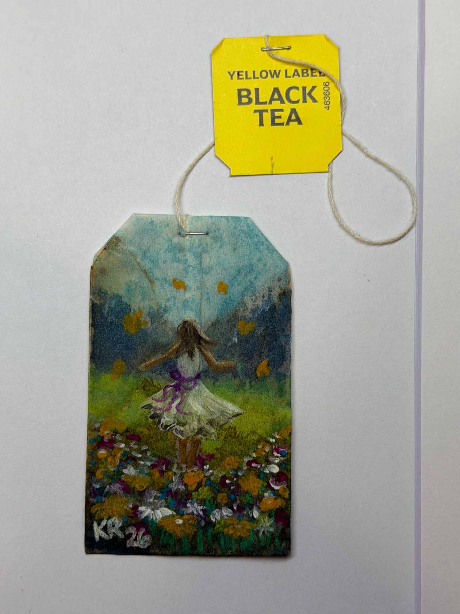 A colorful illustration of a girl dancing in a field of flowers with a cloudy sky background, attached to a yellow label reading 'BLACK TEA'.
