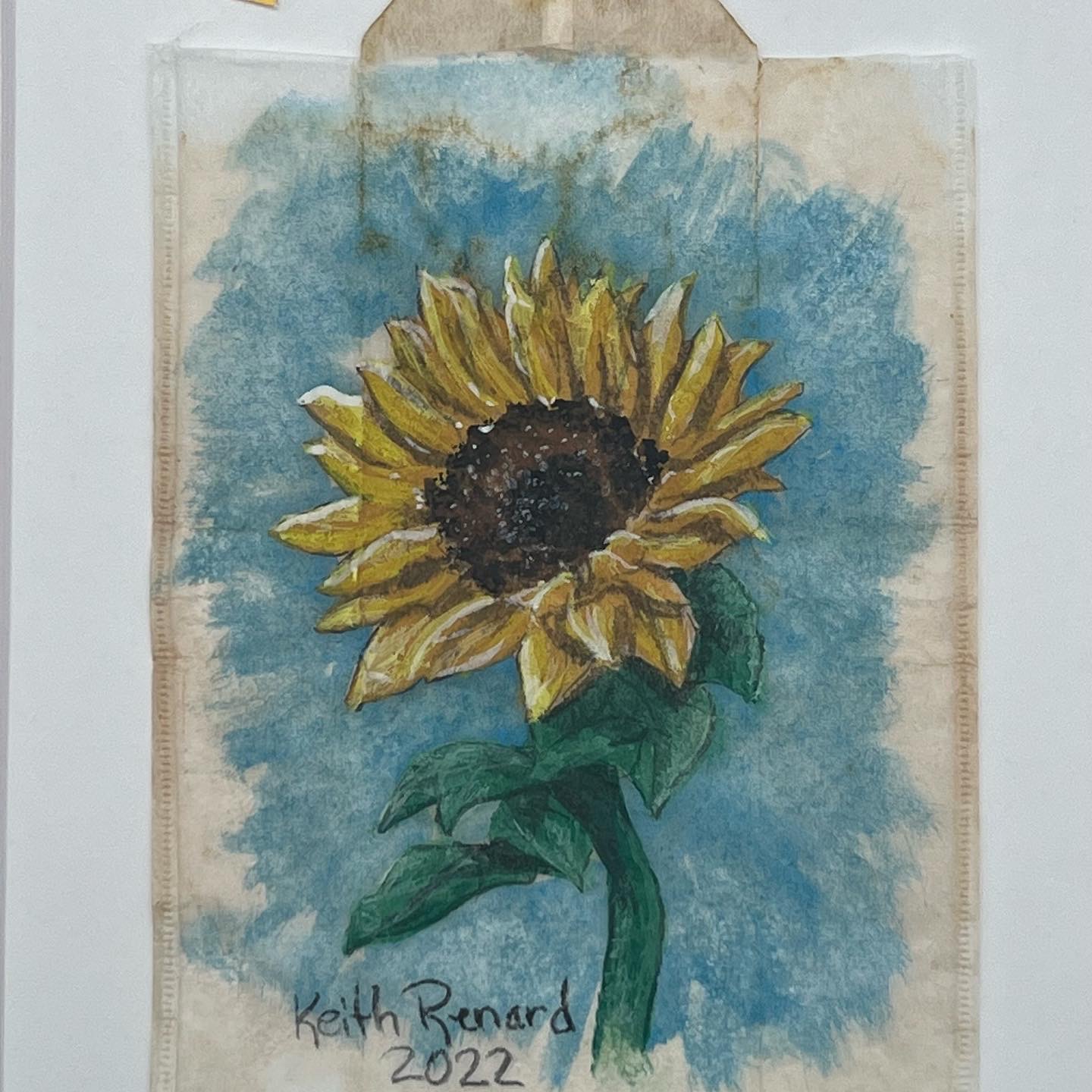 Watercolor painting of a sunflower with yellow petals and green leaves against a blue background, signed by Keith Renard.