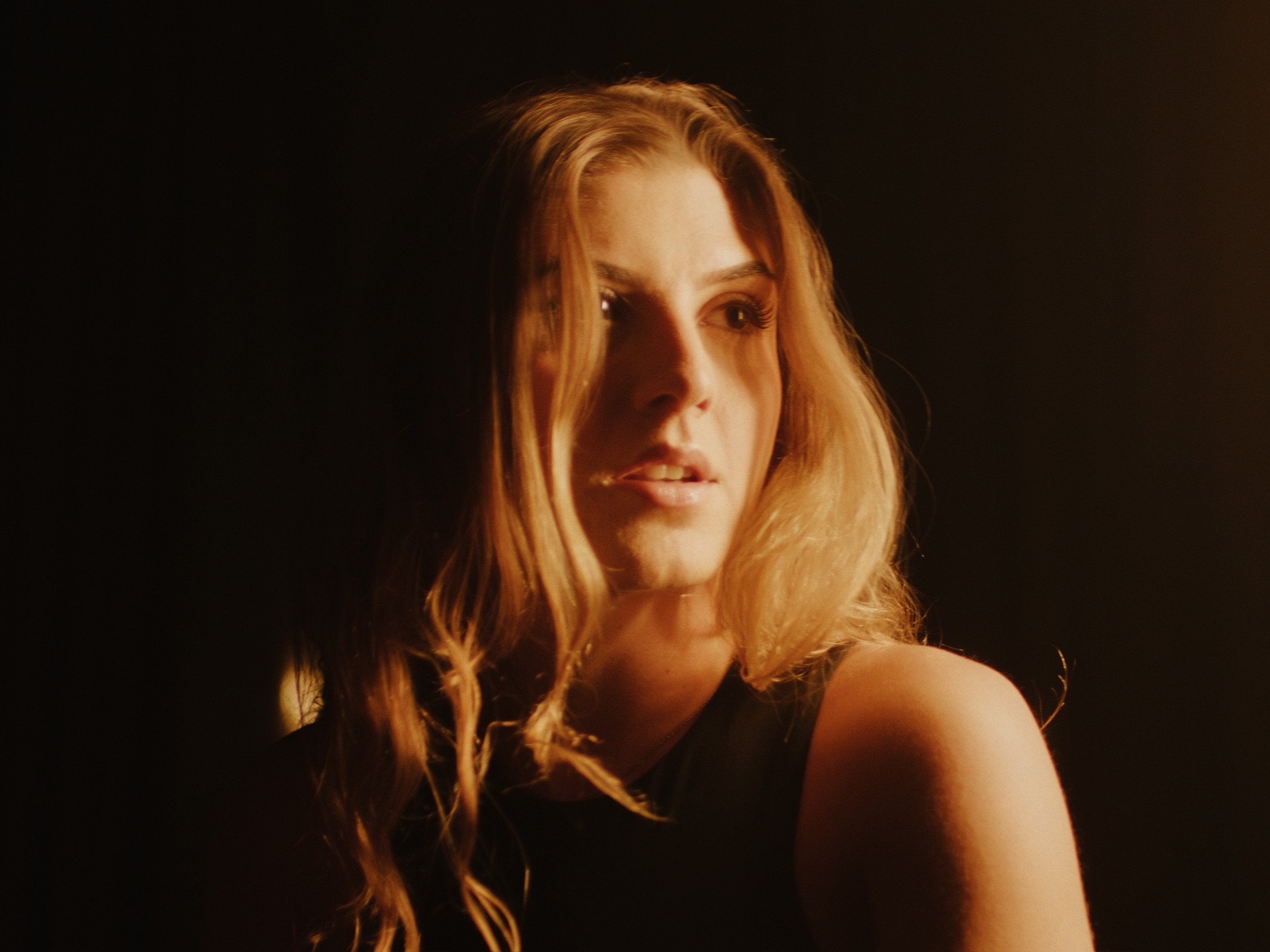 Woman with long hair looking to the side, illuminated by warm light, dark background.