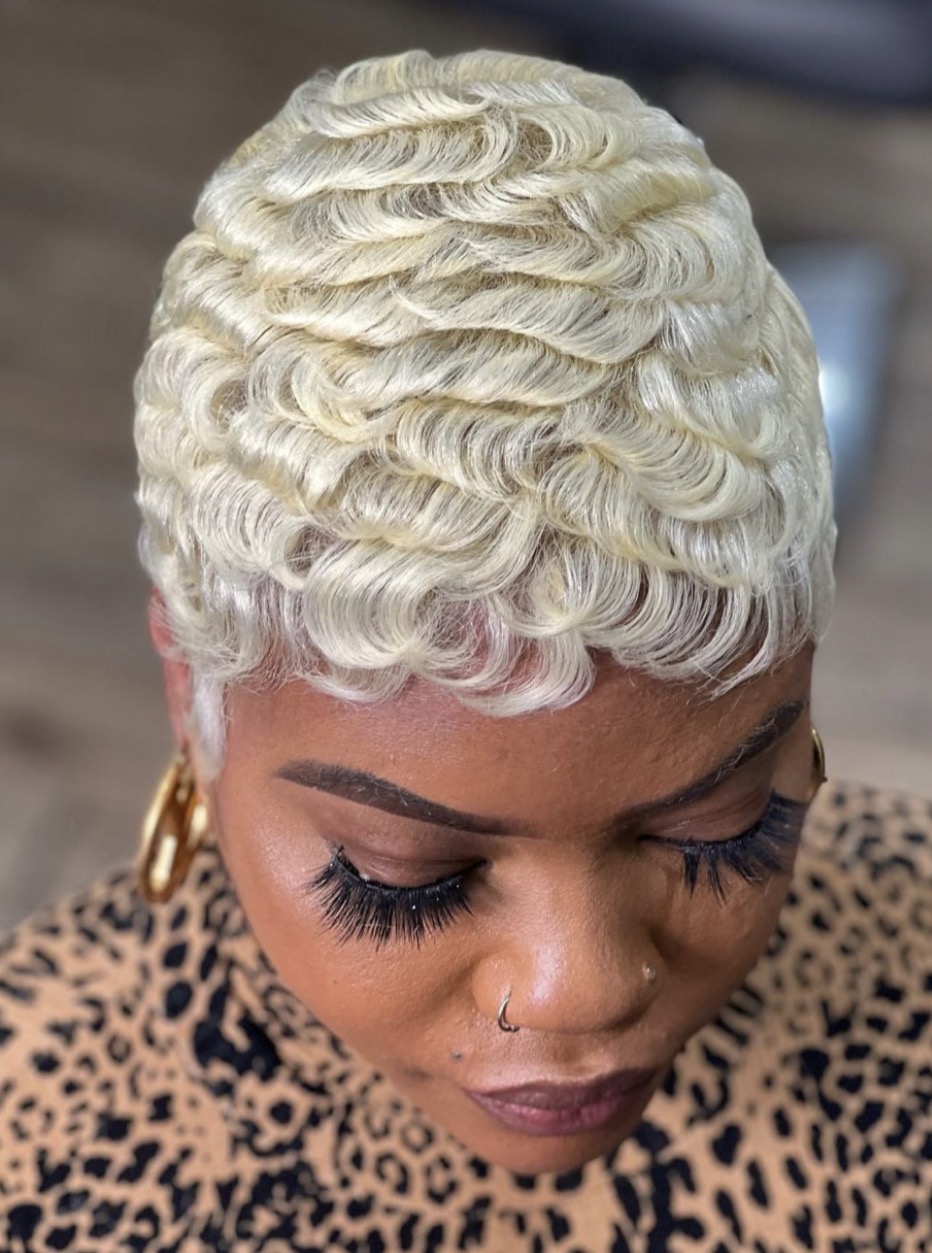 Close-up of a woman with short, platinum blonde, curly hairstyle, wearing leopard print clothing and gold hoop earrings.