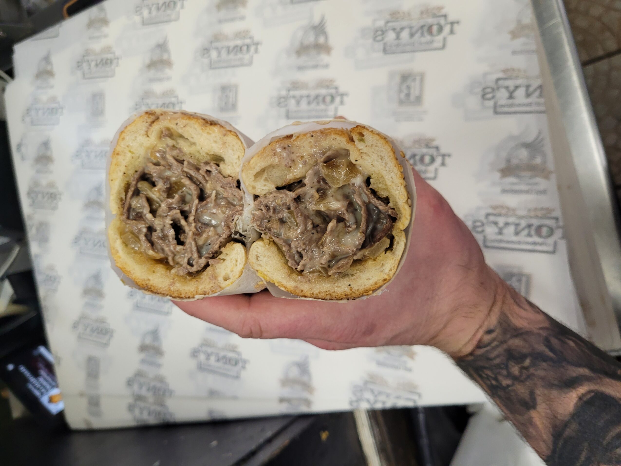 Hand holding a halved pastry with a meat filling, background shows a paper-lined surface.