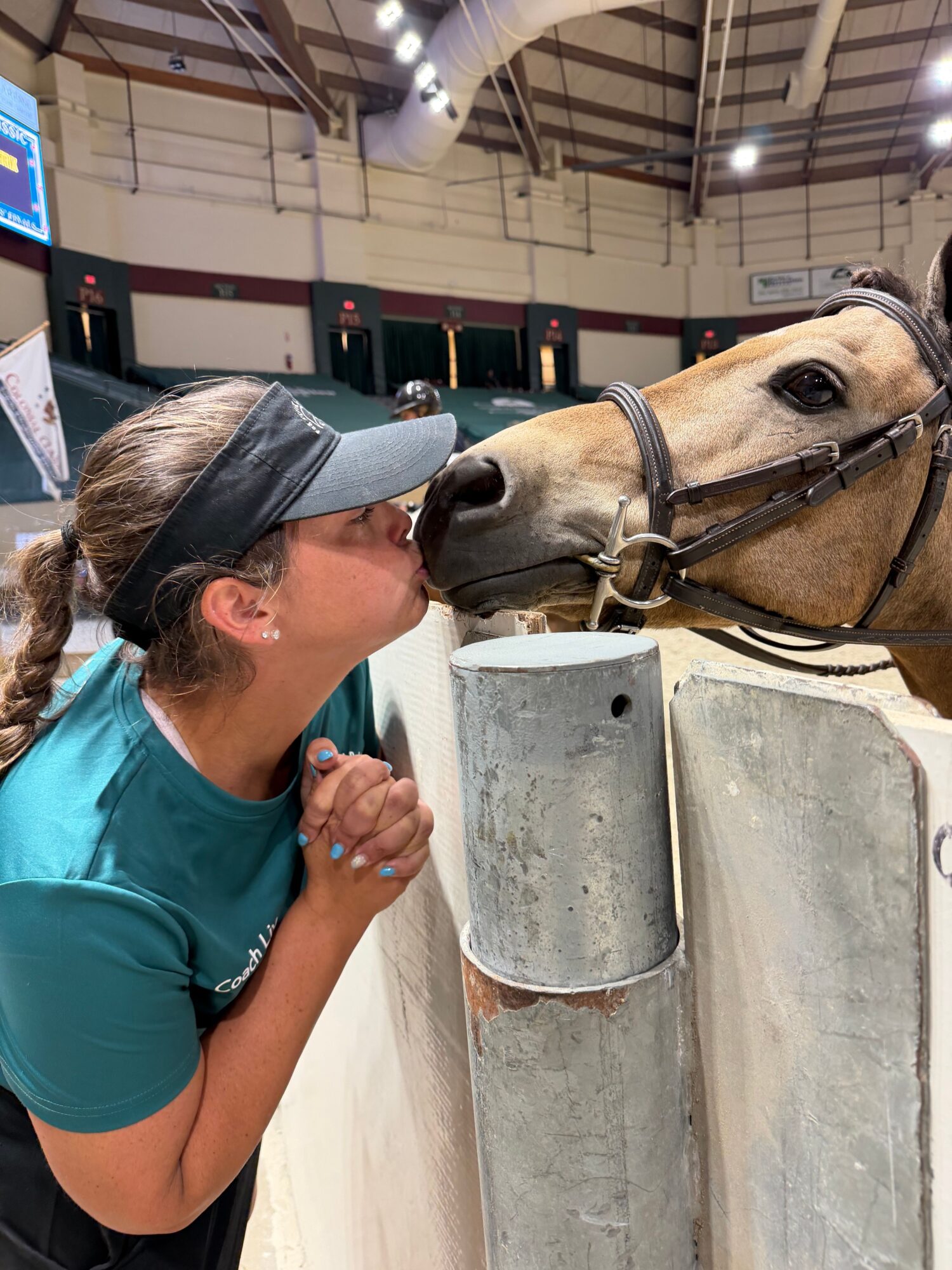 Person lying on the ground with a horse nearby, in an indoor riding arena, concrete blocks in the background.