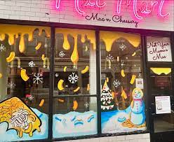 Store window decorated with snowflakes, a snowman, and winter scene, with yellow moon and snow-covered ground, festive holiday display.