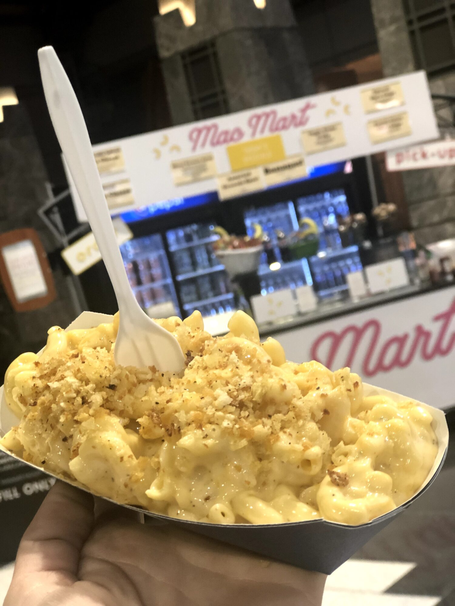 Hand holding a spoonful of yellow ice cream with a store counter in the background.