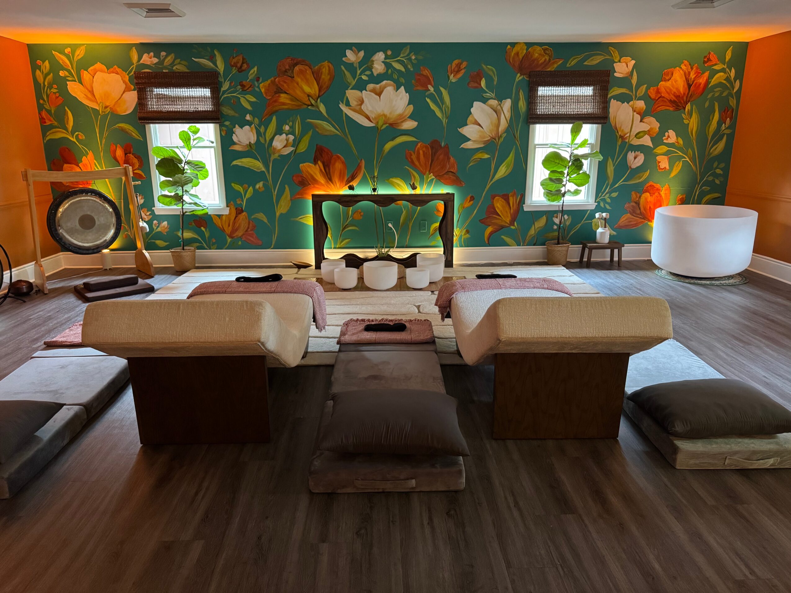 Room with a colorful floral mural wall, two small windows, and meditation cushions on a wooden floor.