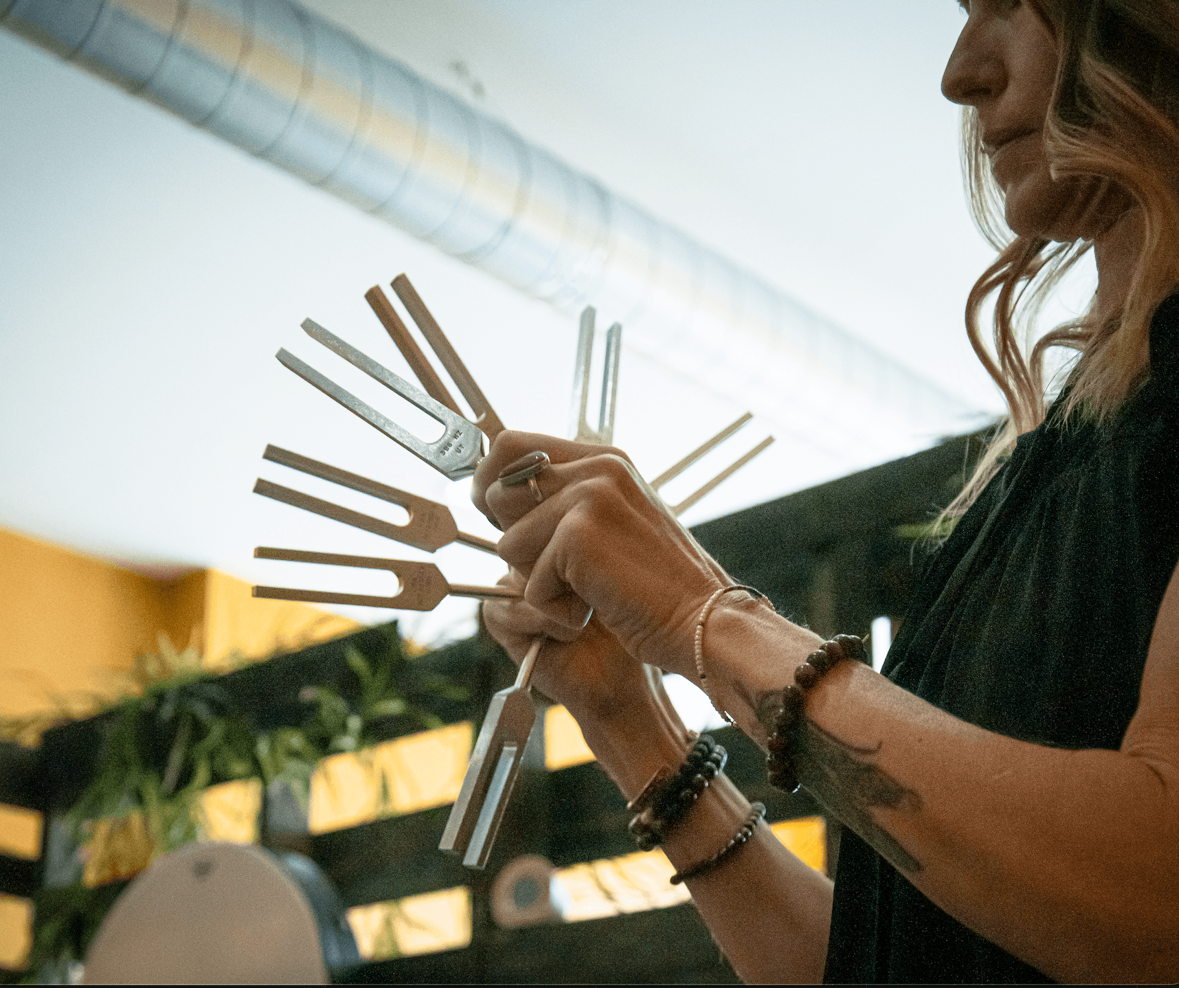 Person holding multiple metal and wooden forks in a restaurant or cafe setting.