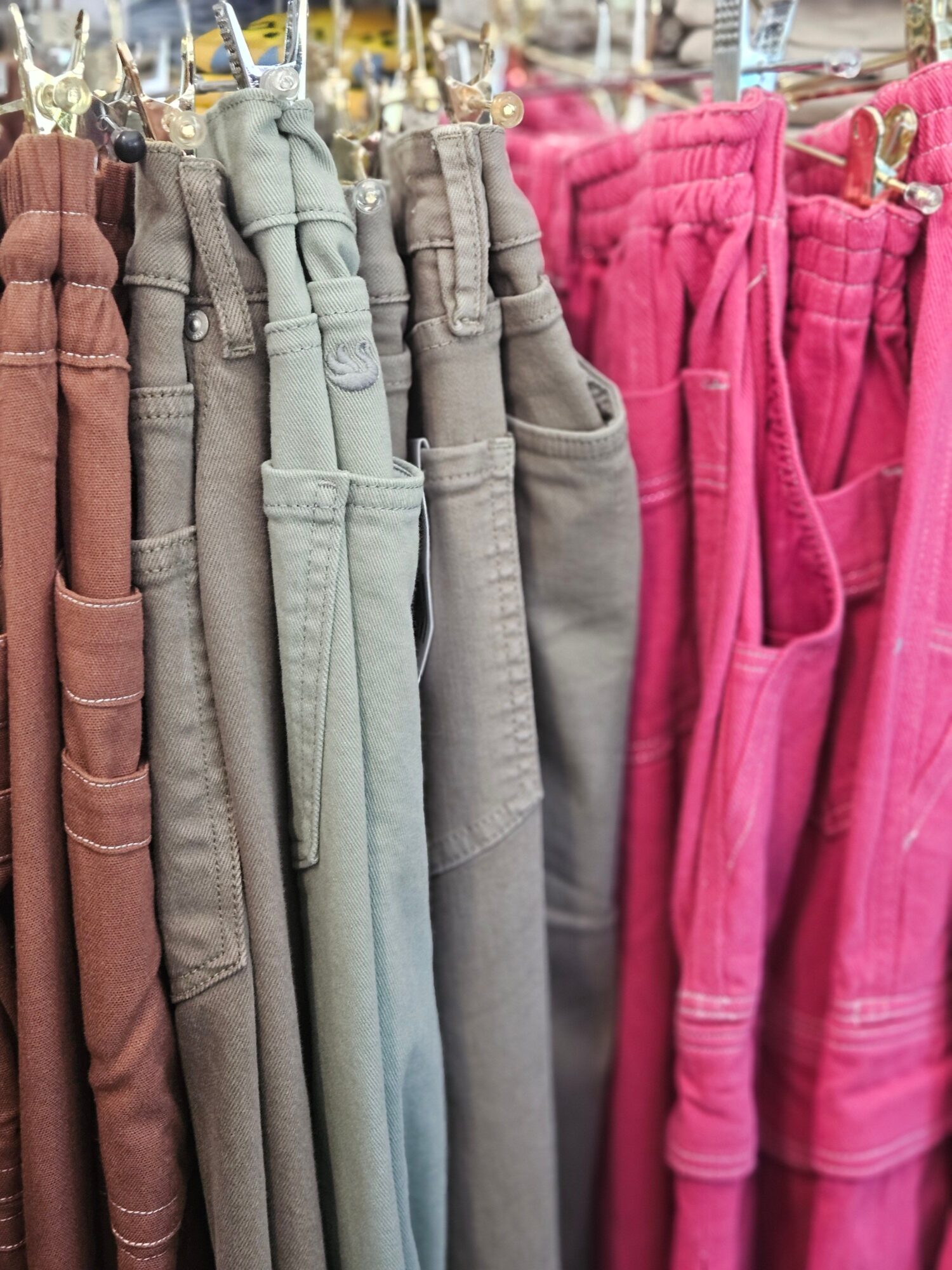 Stack of folded pants in pink, gray, light blue, beige, and brown colors on a store shelf.