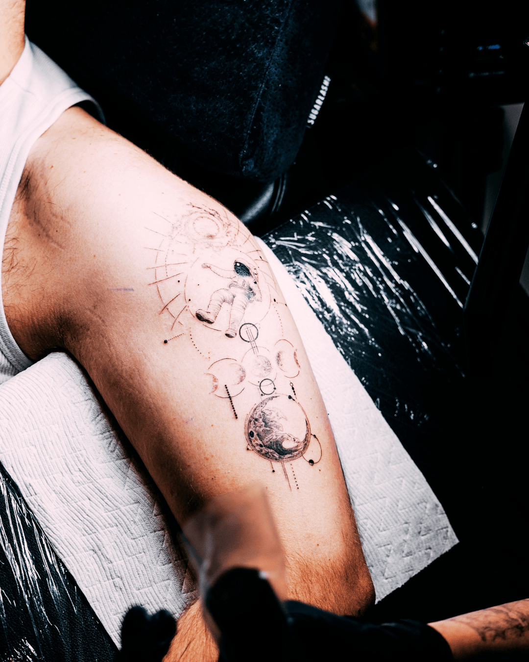 A person's arm with a tattoo design in progress, including a globe and text, on a white surface with black background.