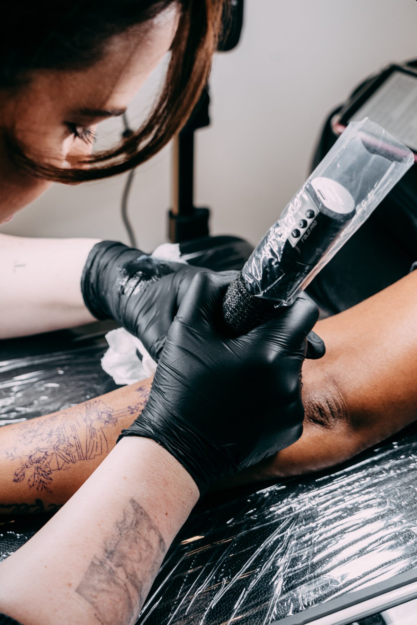 Tattoo artist wearing black gloves applying ink to a person's arm with a tattoo machine.