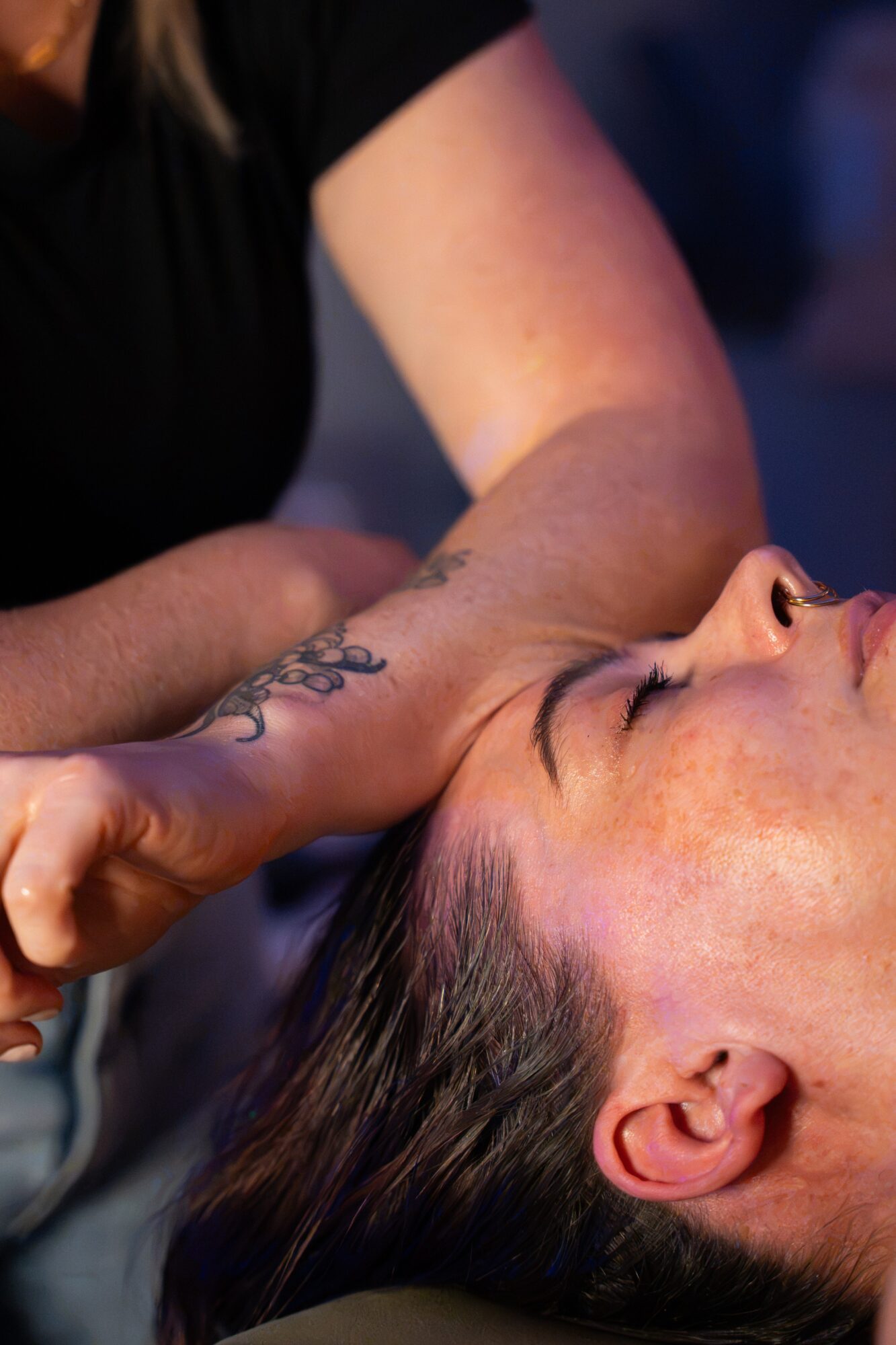 Person receiving a massage with a focus on the arm and face, lying down with eyes closed.