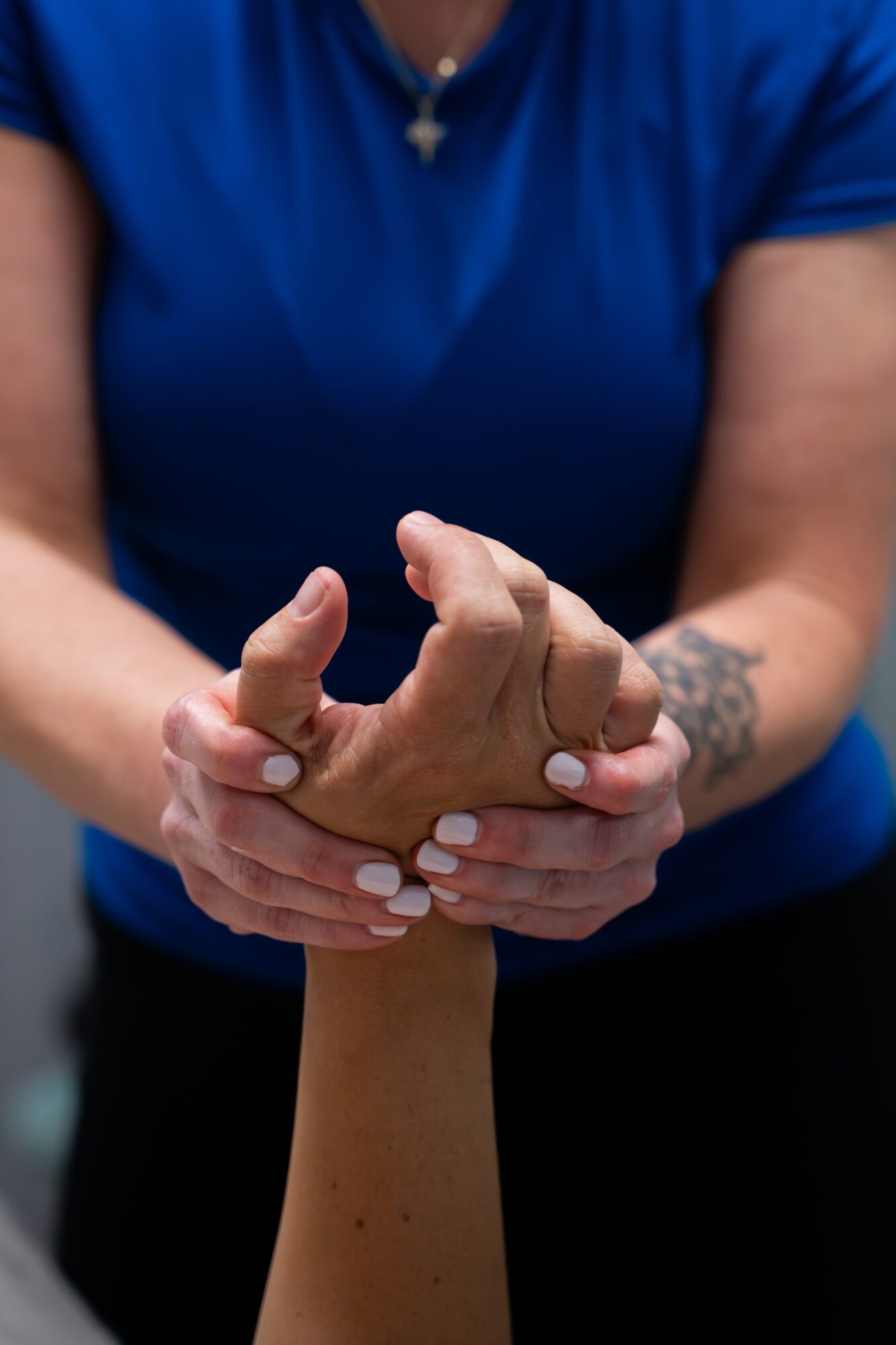 Person with tattoo on arm holding another person's hand, both with visible nails, against a dark background.