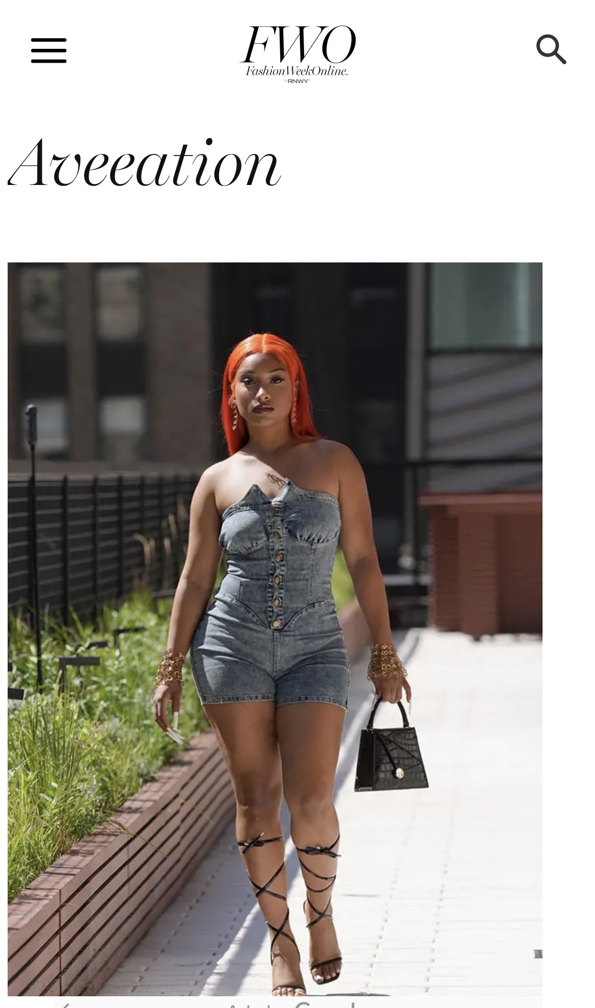 Woman with red hair in denim romper and lace-up heels walking outdoors, holding a black handbag.