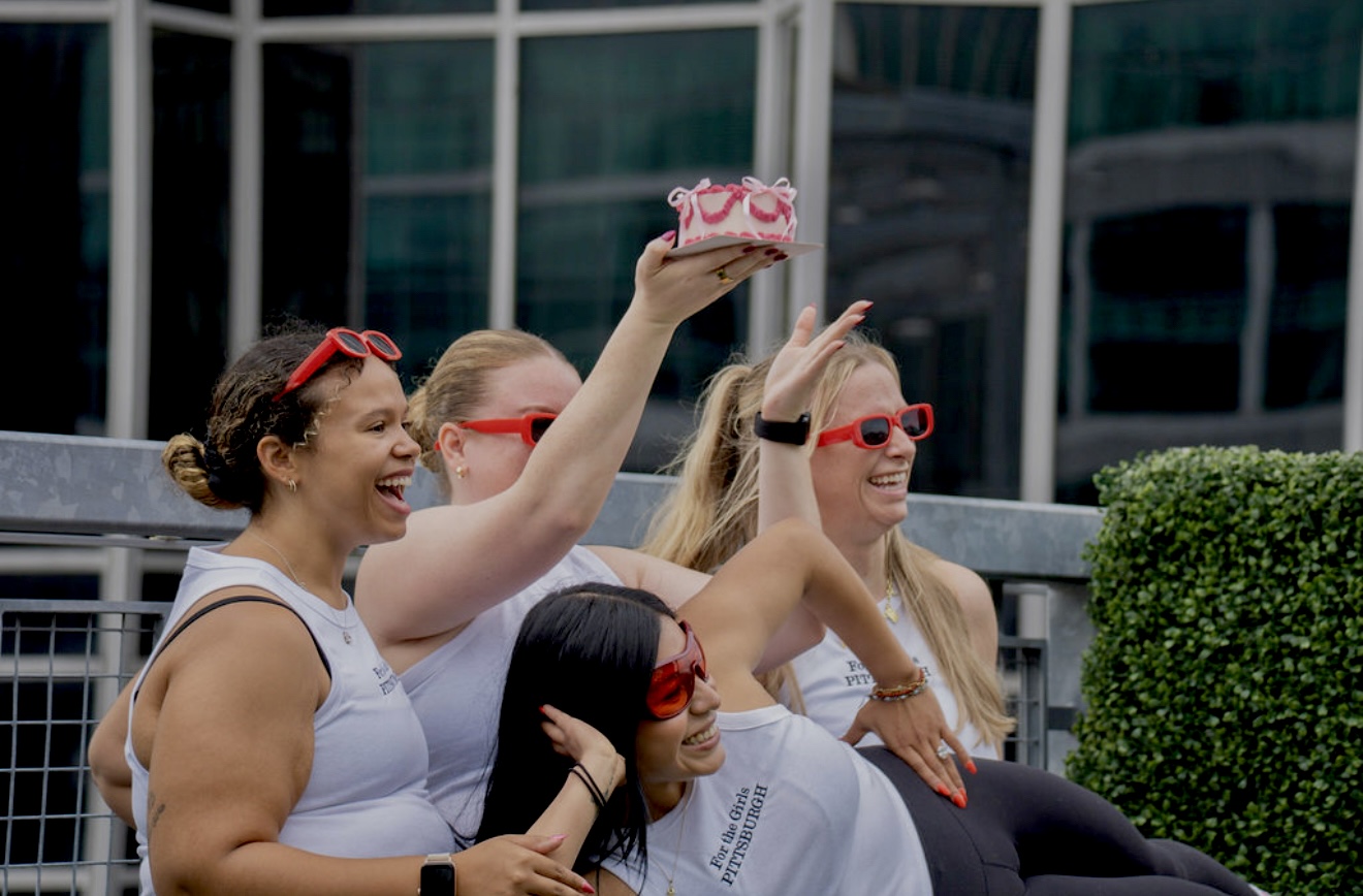 Four women sitting outdoors, one holding a cake, all wearing sunglasses and smiling.