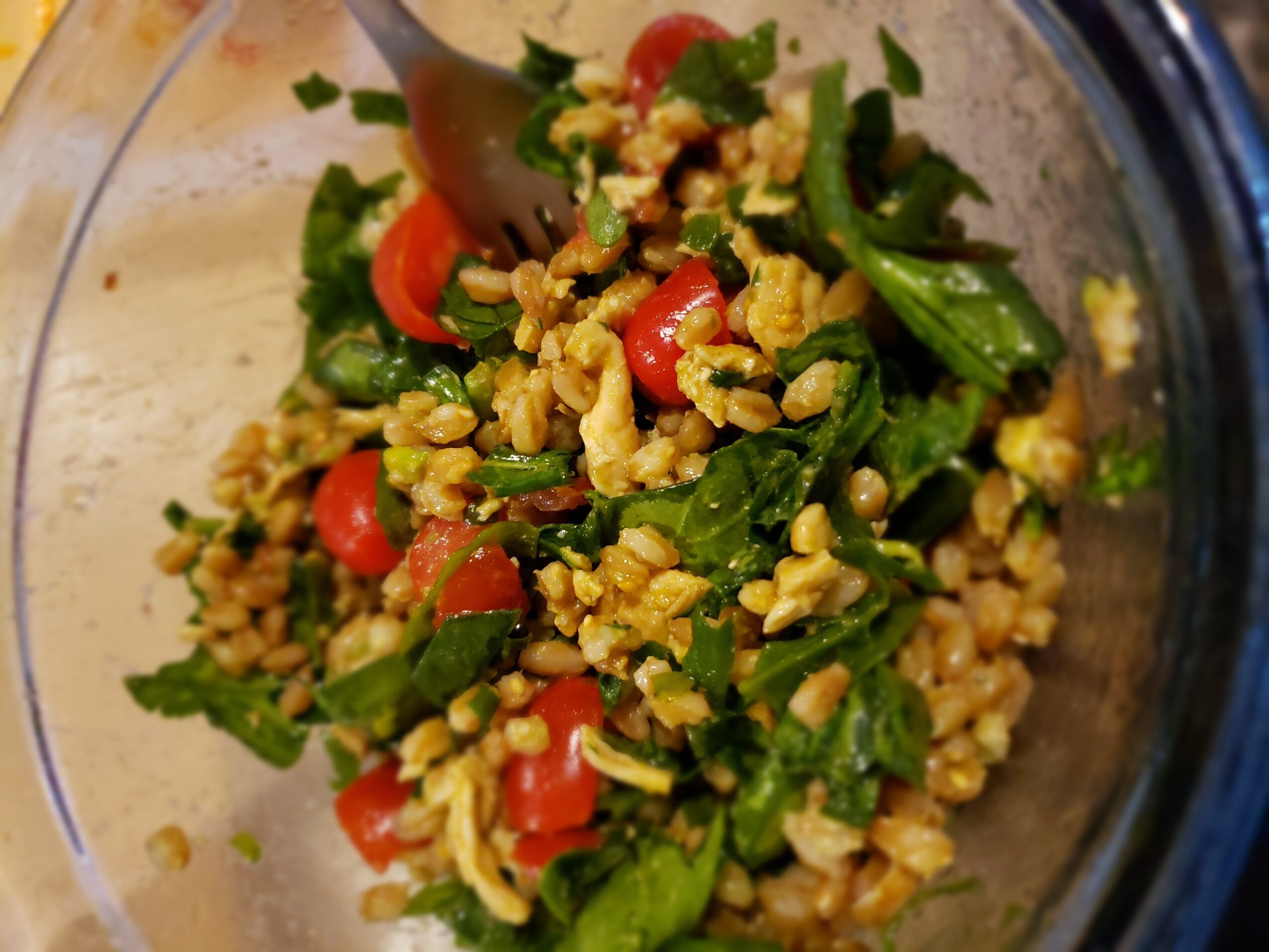 Mixed salad with chopped greens, cherry tomatoes, and scrambled eggs in a glass bowl, with a spoon inside.
