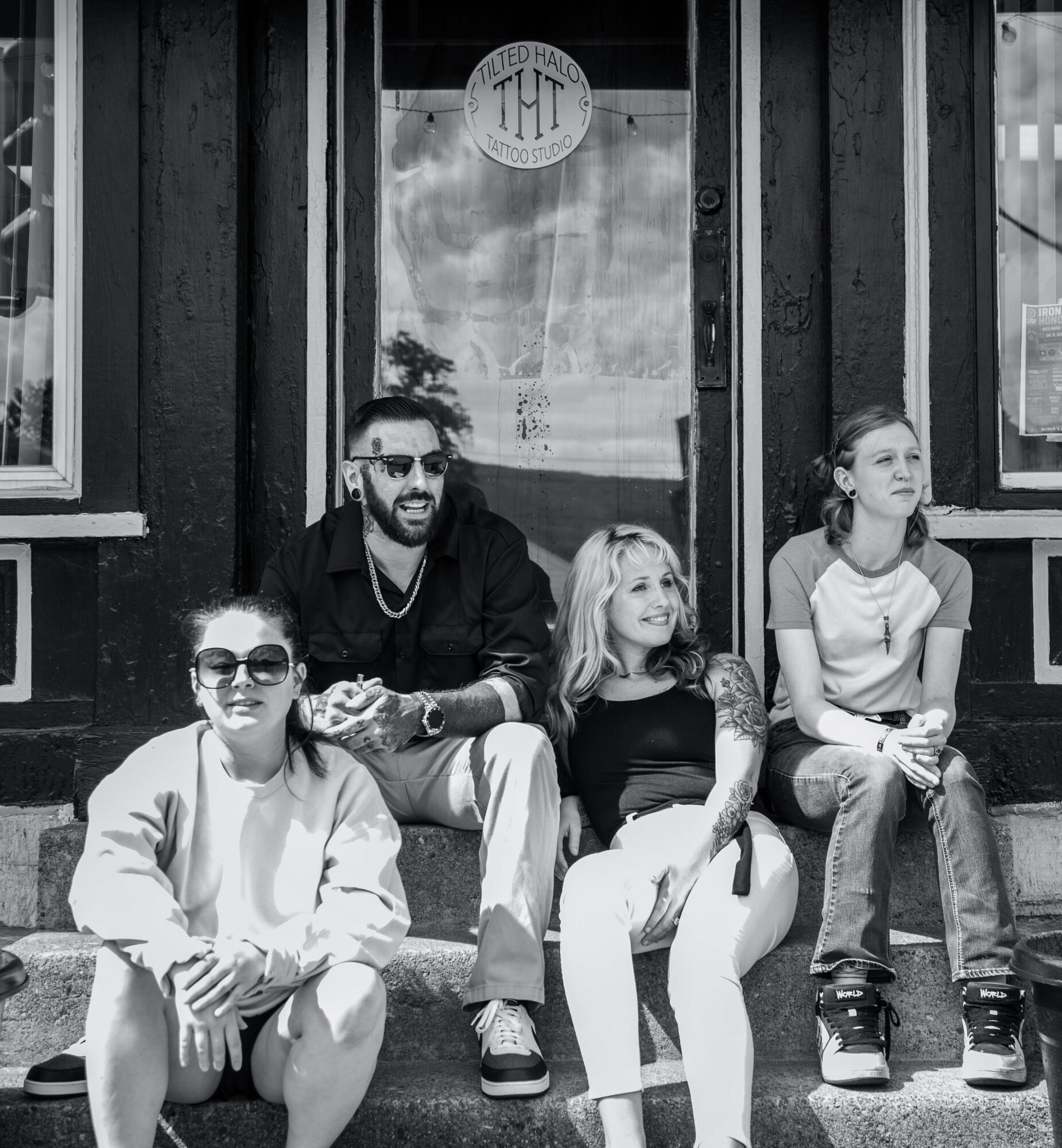 Four people sitting on a step outside a building, smiling and looking in different directions.