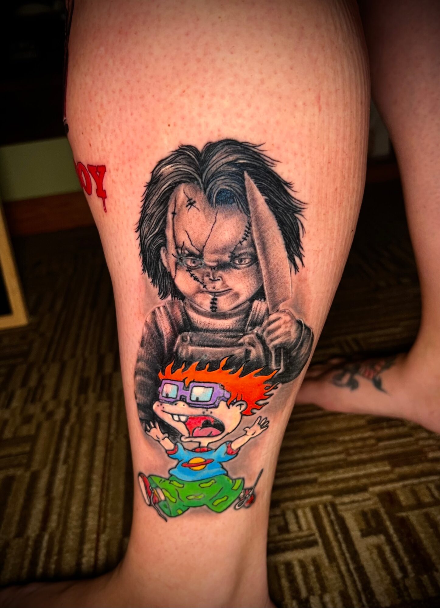 Tattoo of a cartoon character with spiky orange hair, glasses, and a distressed expression, holding a baseball bat, on a person's leg.
