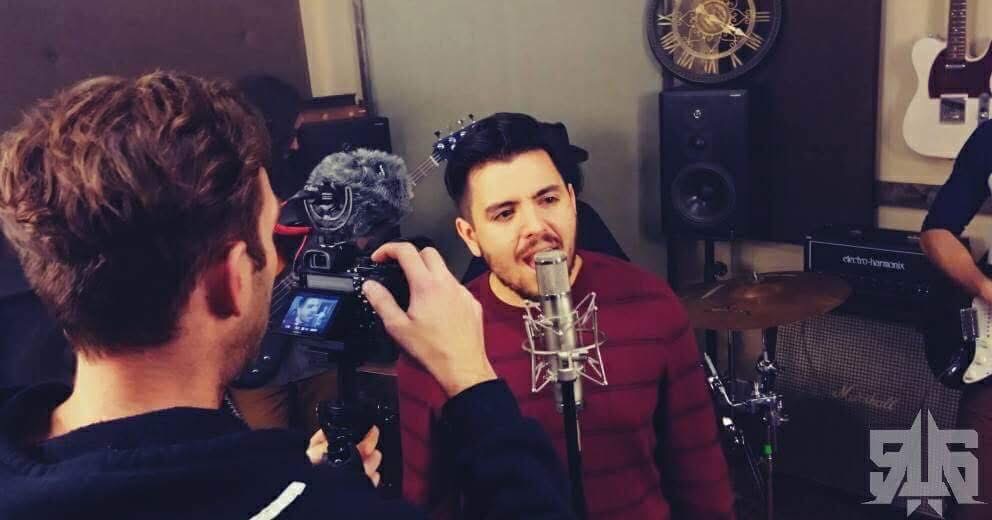 Person with curly hair records a man singing into a microphone in a music studio.
