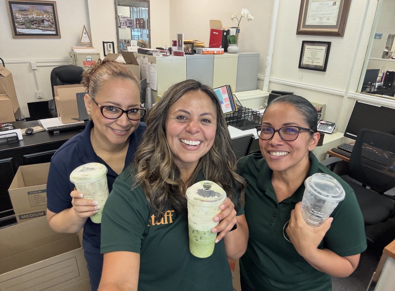 Three women smiling and holding cups of ice cream in an office setting.
