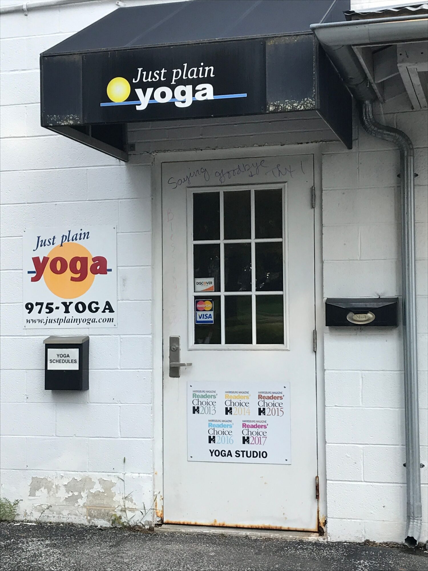 White door with signs and a window, next to a black sign that says 'Just plain yoga,' on a white wall.