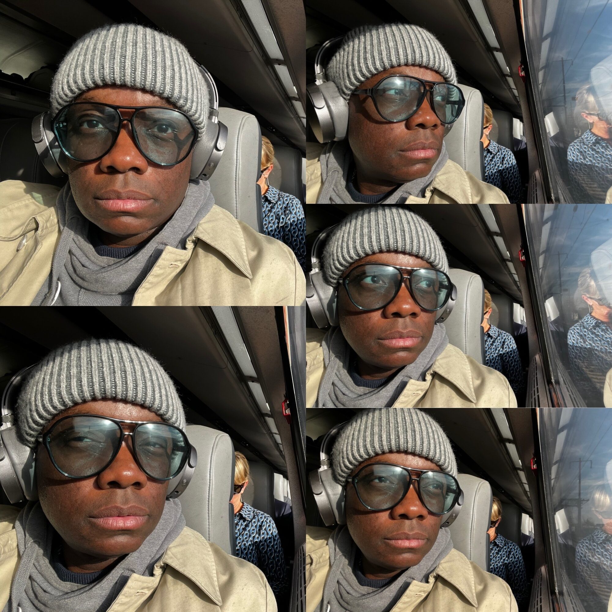Person wearing a gray beanie, sunglasses, headphones, and a beige jacket, sitting on a bus with windows and other passengers visible.