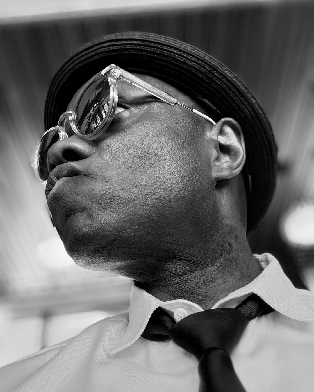 Man wearing glasses, hat, and tie, looking to the side, in black and white.