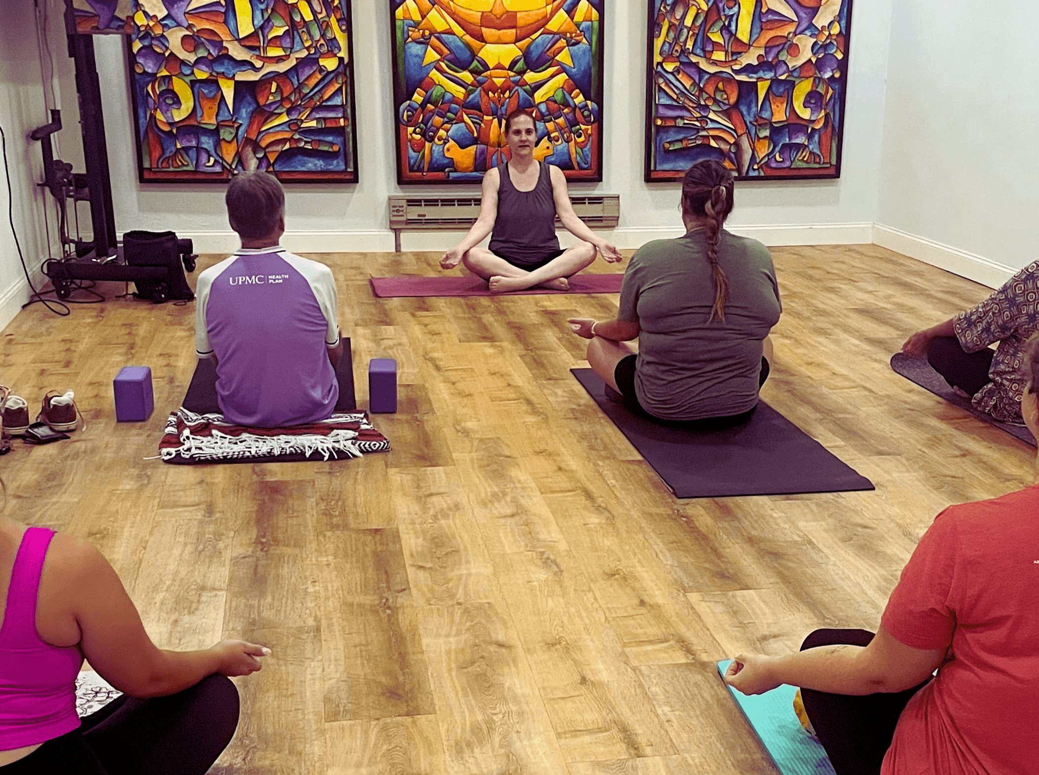 Group of people participating in a yoga class in a room with colorful abstract artwork on the wall.