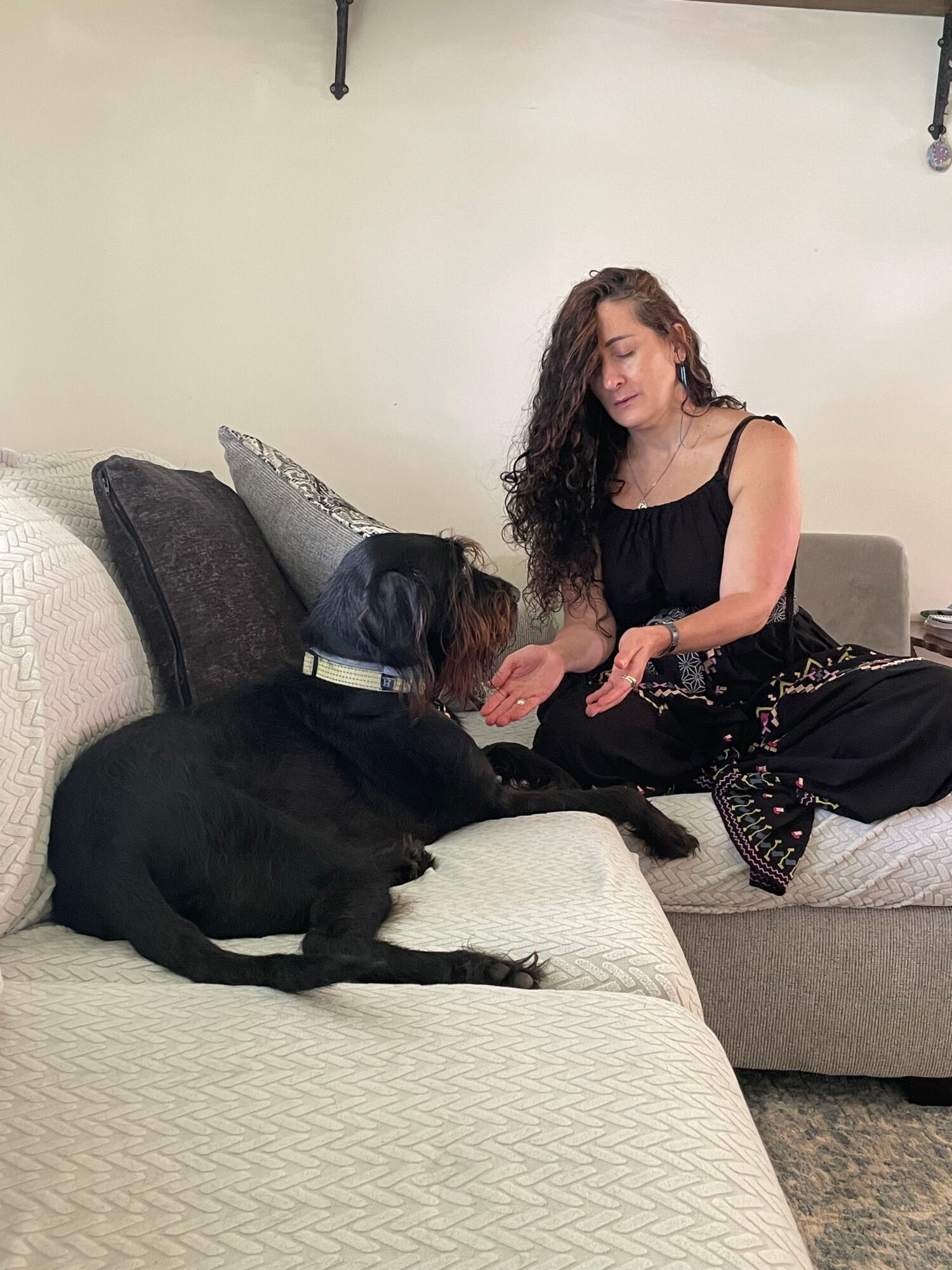 Two women and a black dog on a couch in a living room, one woman sitting and the other lying down.
