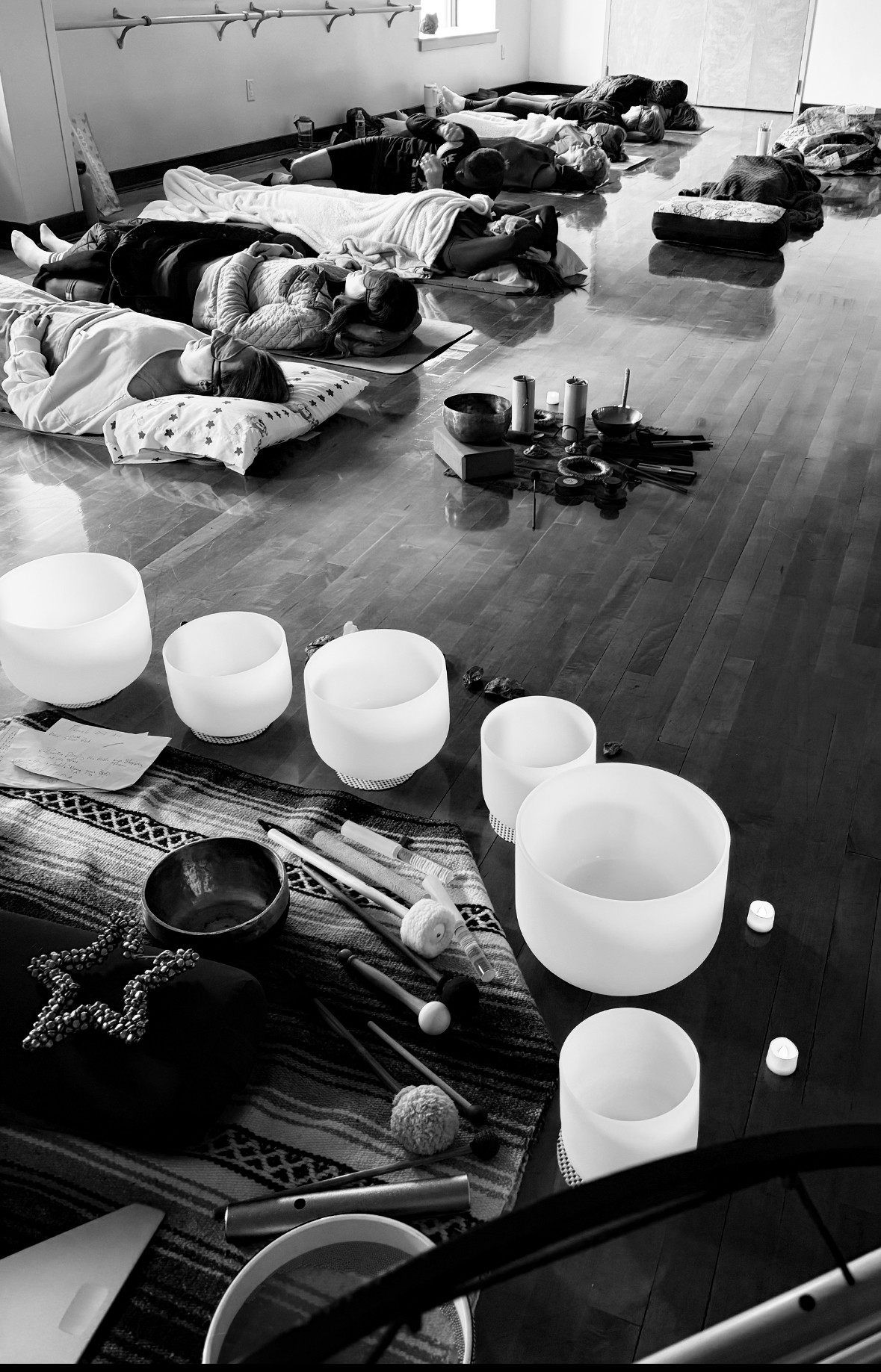 People lying on mats in a room, with glowing bowls and objects on a table in the foreground.