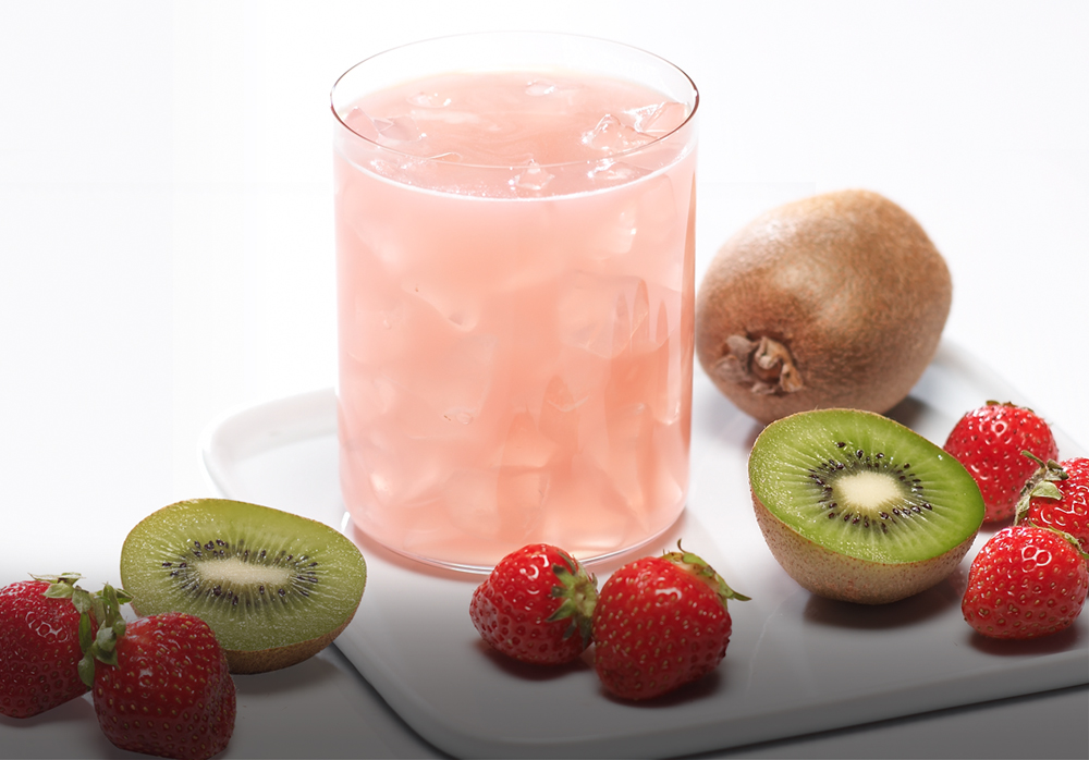 A glass of pink smoothie surrounded by strawberries, kiwi slices, a whole kiwi, and a small round fruit, on a white surface.