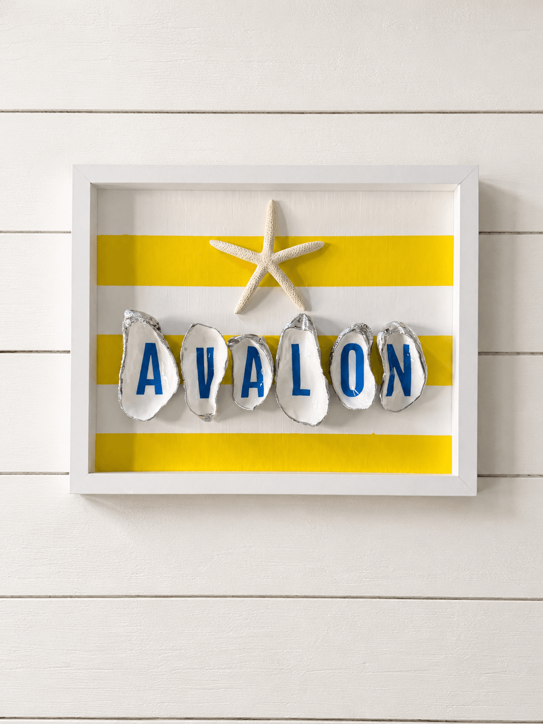 Decorative wall display with yellow and white striped background, starfish, and lettered ornaments spelling 'AVALON'.