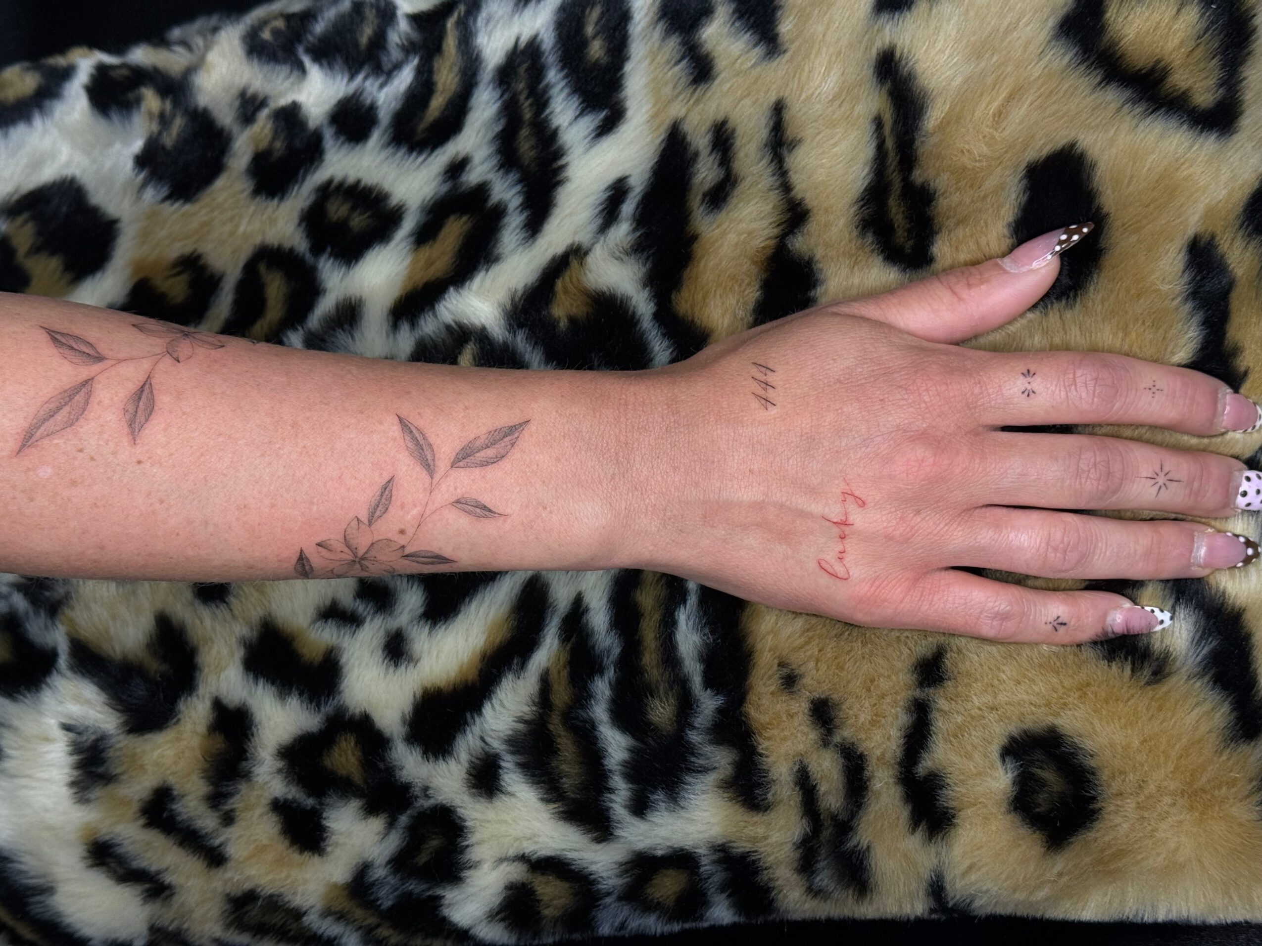 A hand with a tattoo of leaves on the forearm rests on a leopard print fabric.