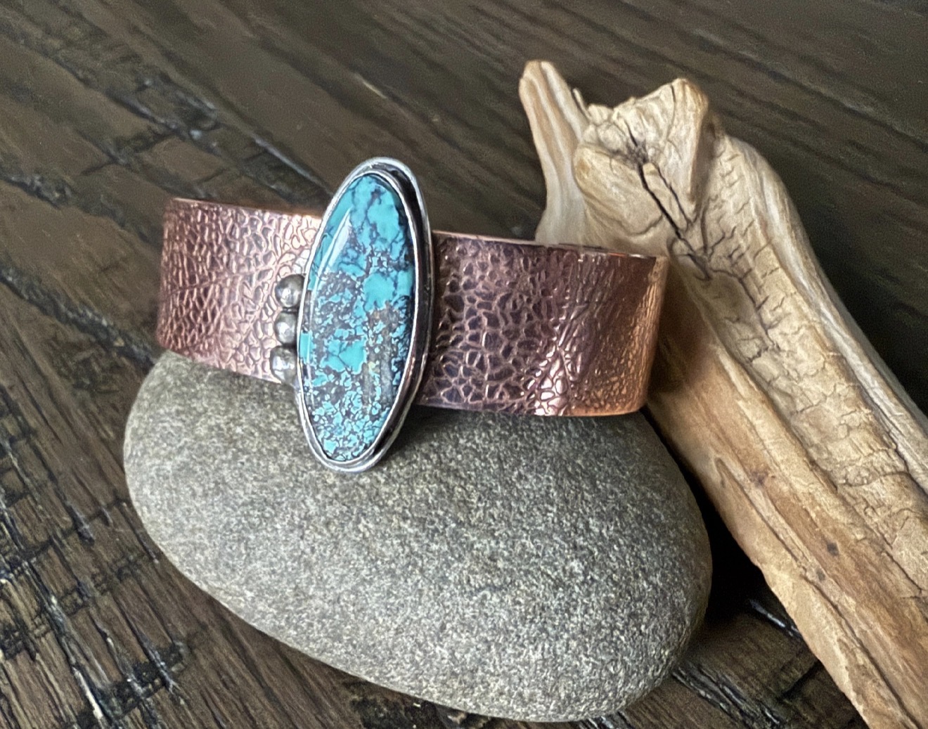 Leather bracelet with turquoise stone, stone, and wood piece on wooden surface.