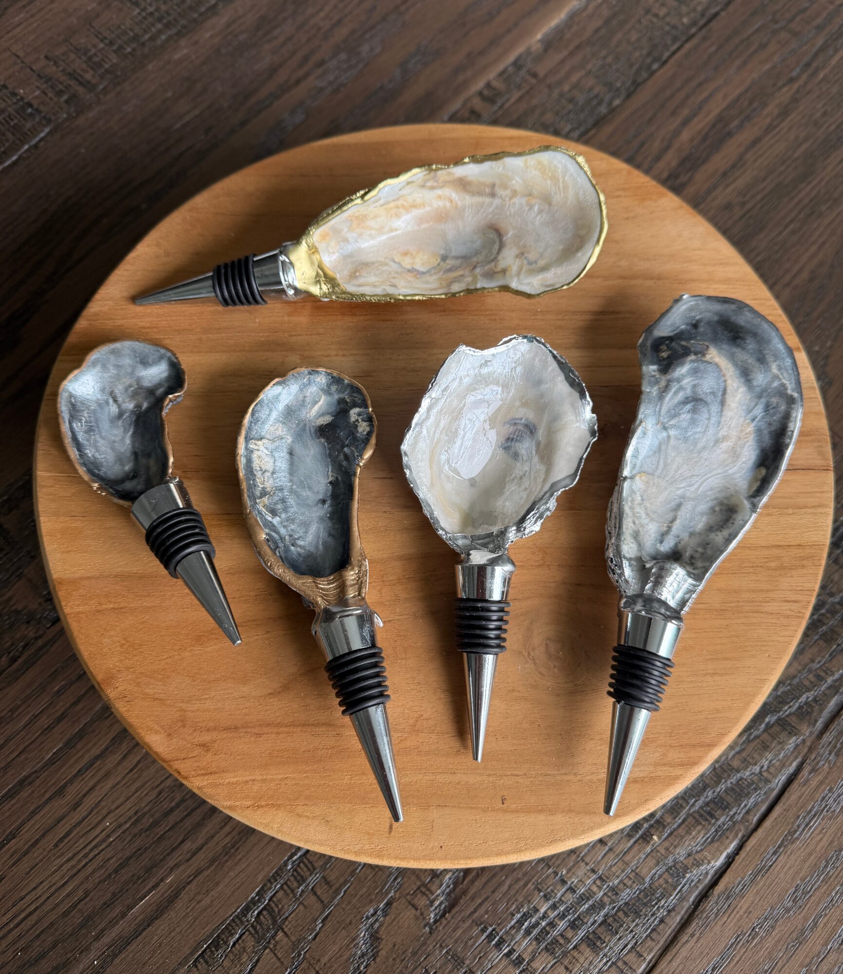 Five opened oyster shells on a round wooden plate, with a dark wooden surface background.