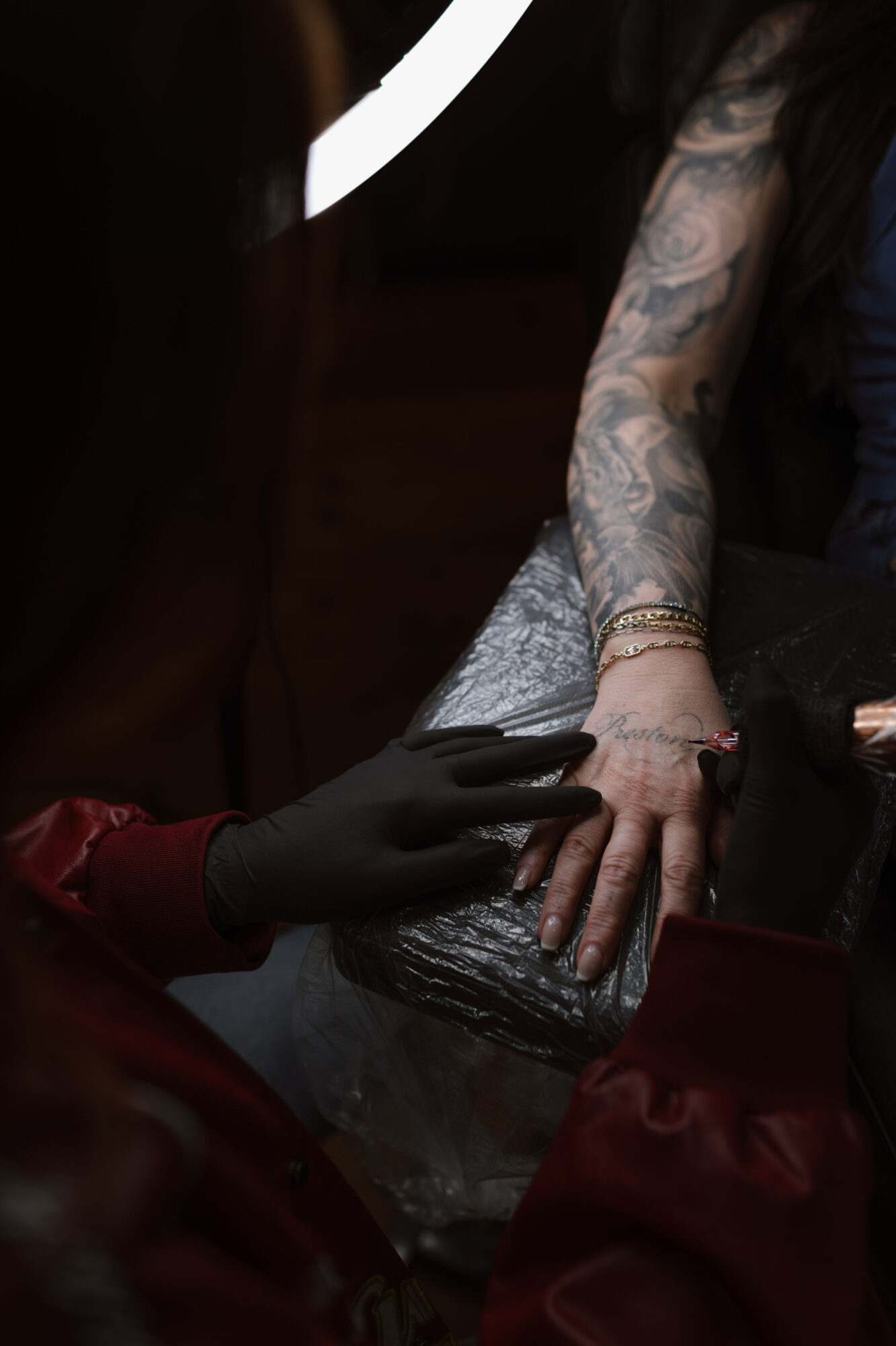 Person with tattooed arm receiving a tattoo, hand resting on a surface, tattoo artist wearing black gloves working.