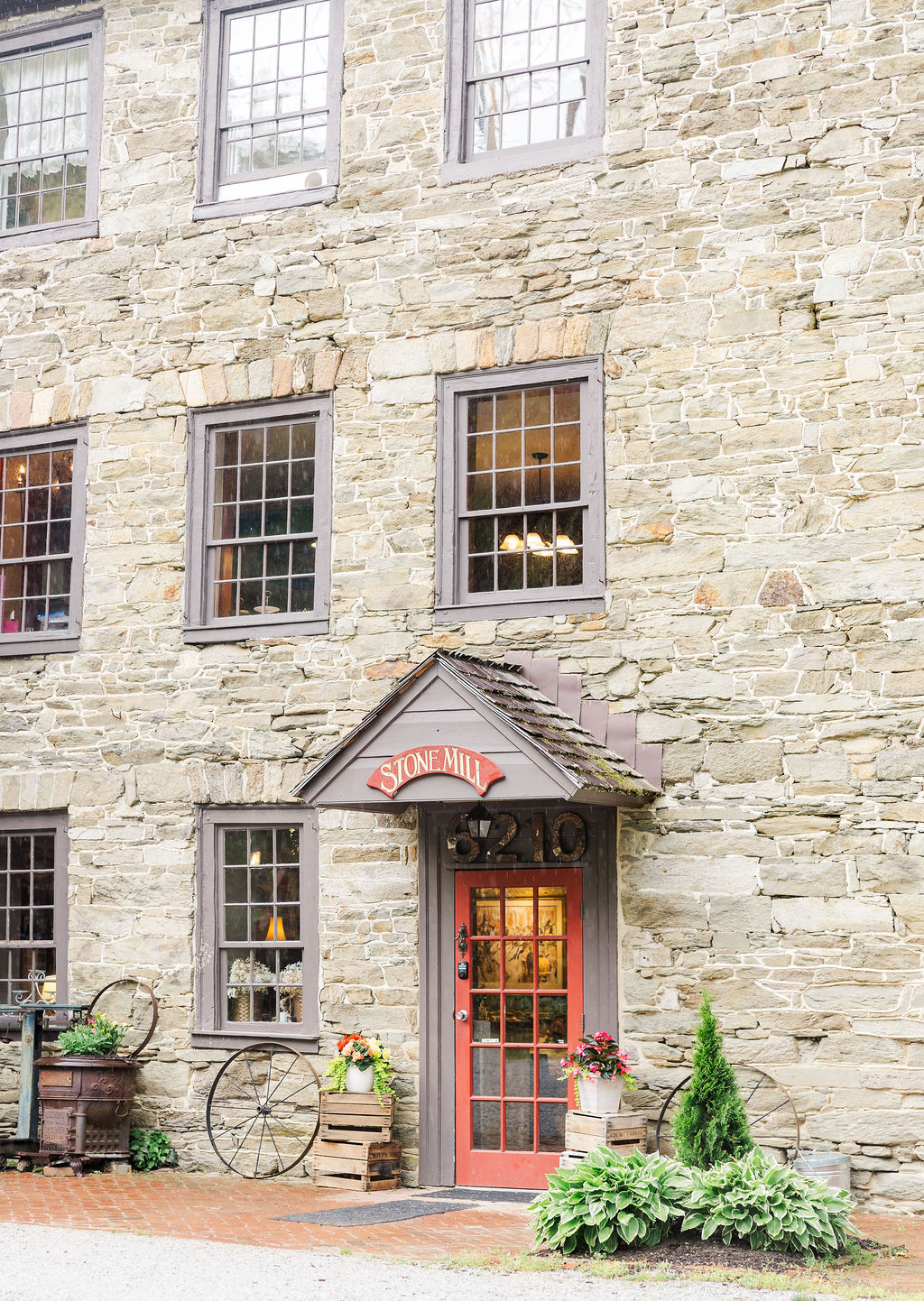 Stone building with multiple windows and a red door, decorated with plants and a bicycle outside.