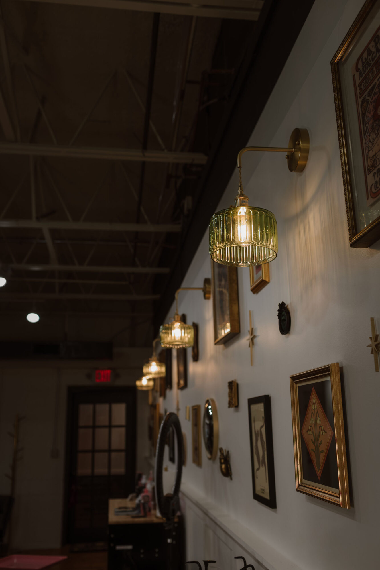Interior wall decorated with framed artwork and hanging lamps, with a door visible in the background.