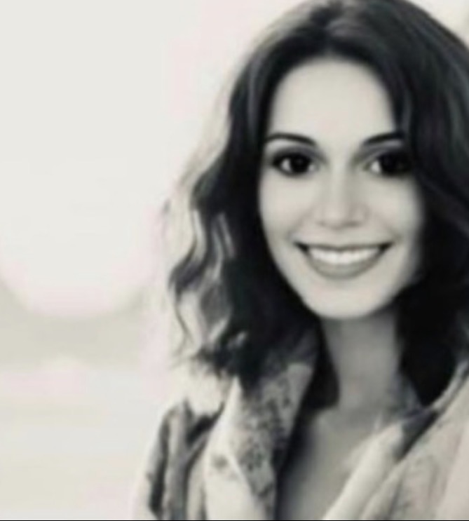 A smiling woman with wavy hair, wearing a jacket, facing the camera in black and white.