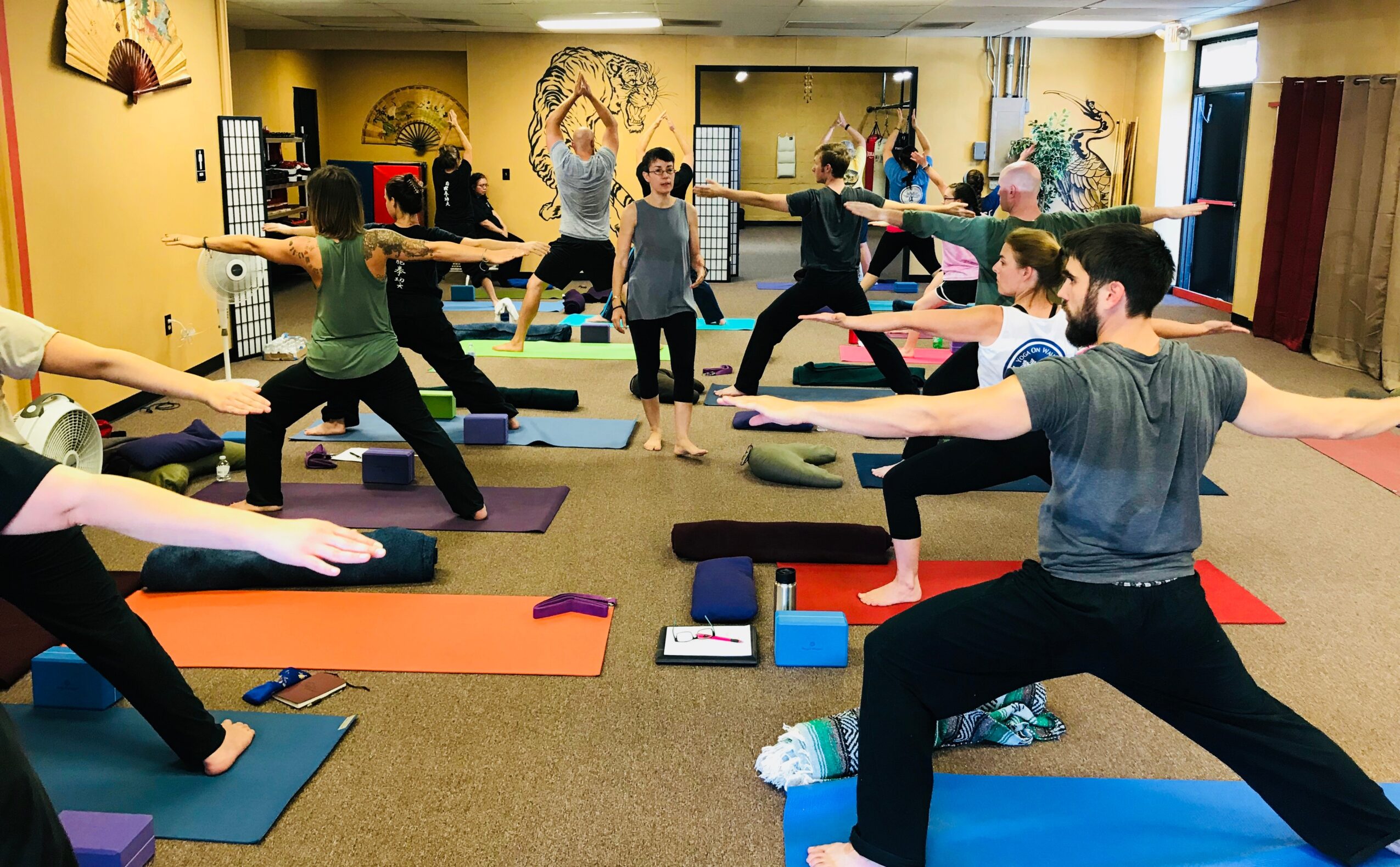 Group of people practicing yoga in a studio with colorful wall art and mirrors, on mats with blocks and straps.