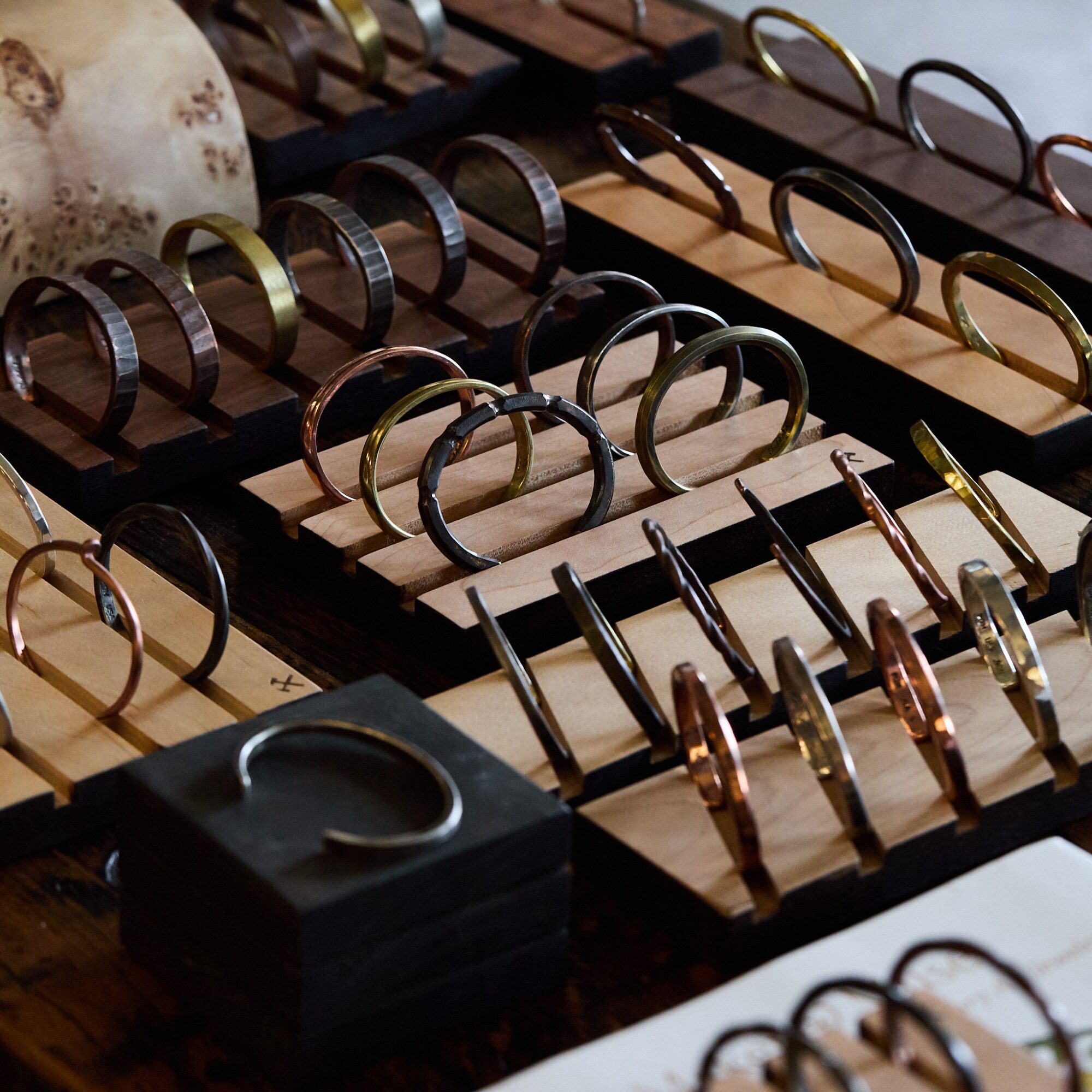 Display of various metal and wooden bracelets and bangles on wooden trays, with a black box in the foreground.