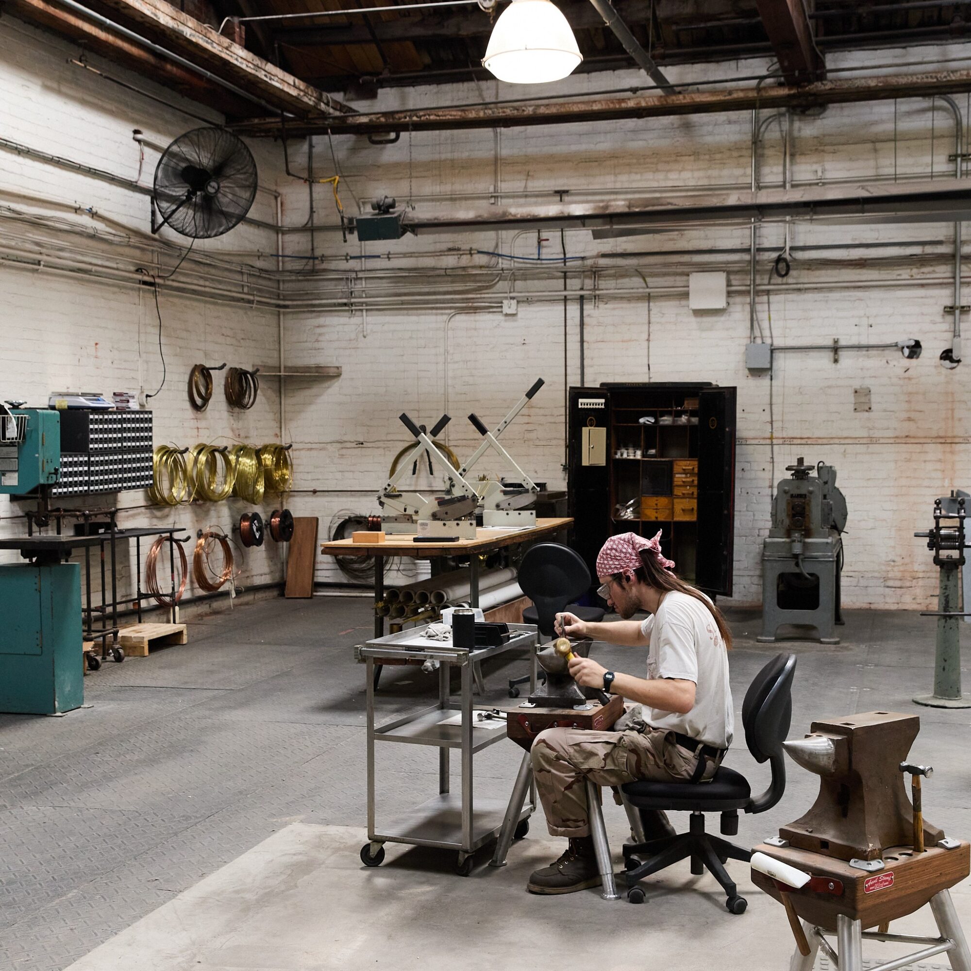 Person working with machinery in a workshop with tools and equipment on walls and shelves.